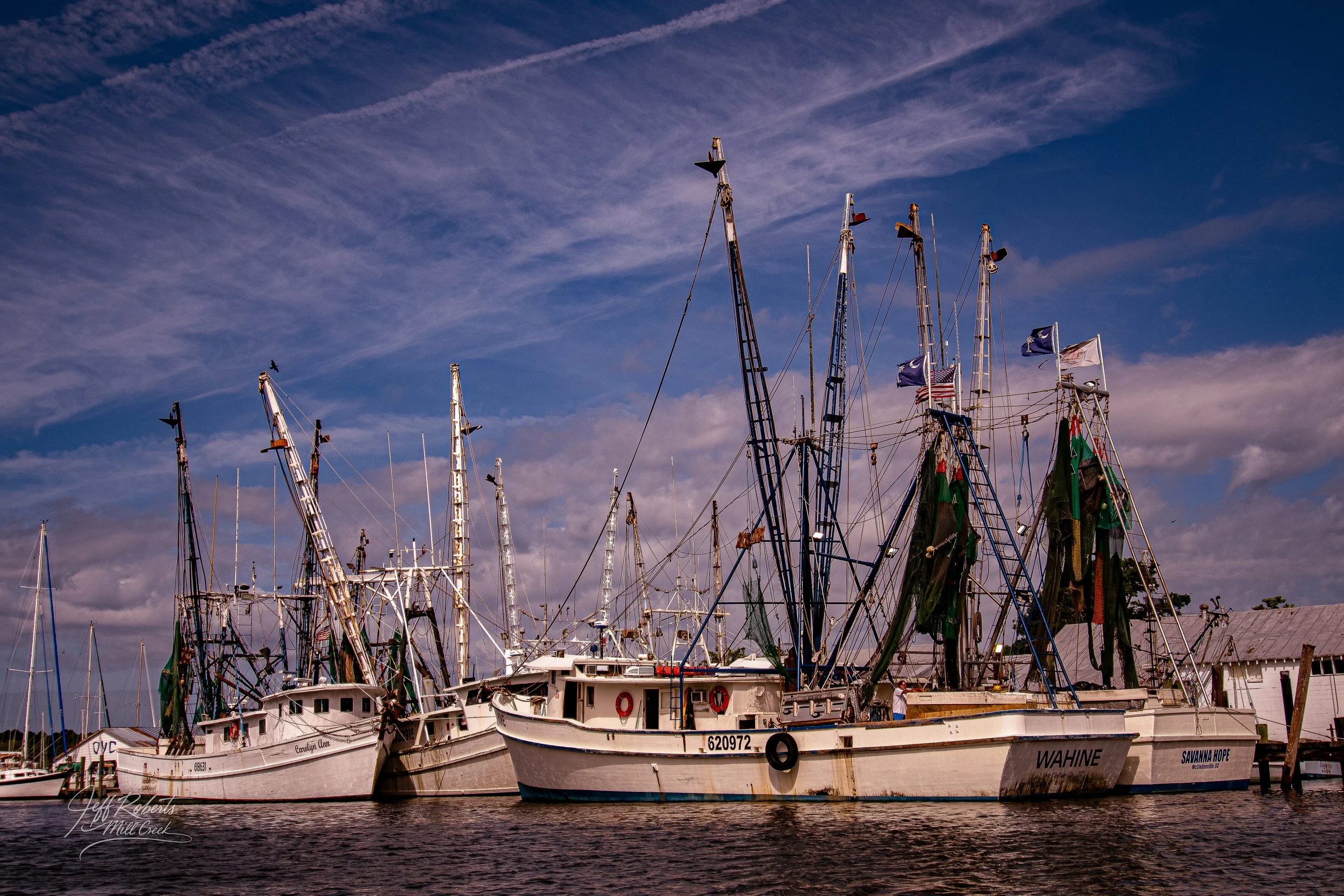 Several fishing boats docked at a harbor with a cloudy sky overhead.