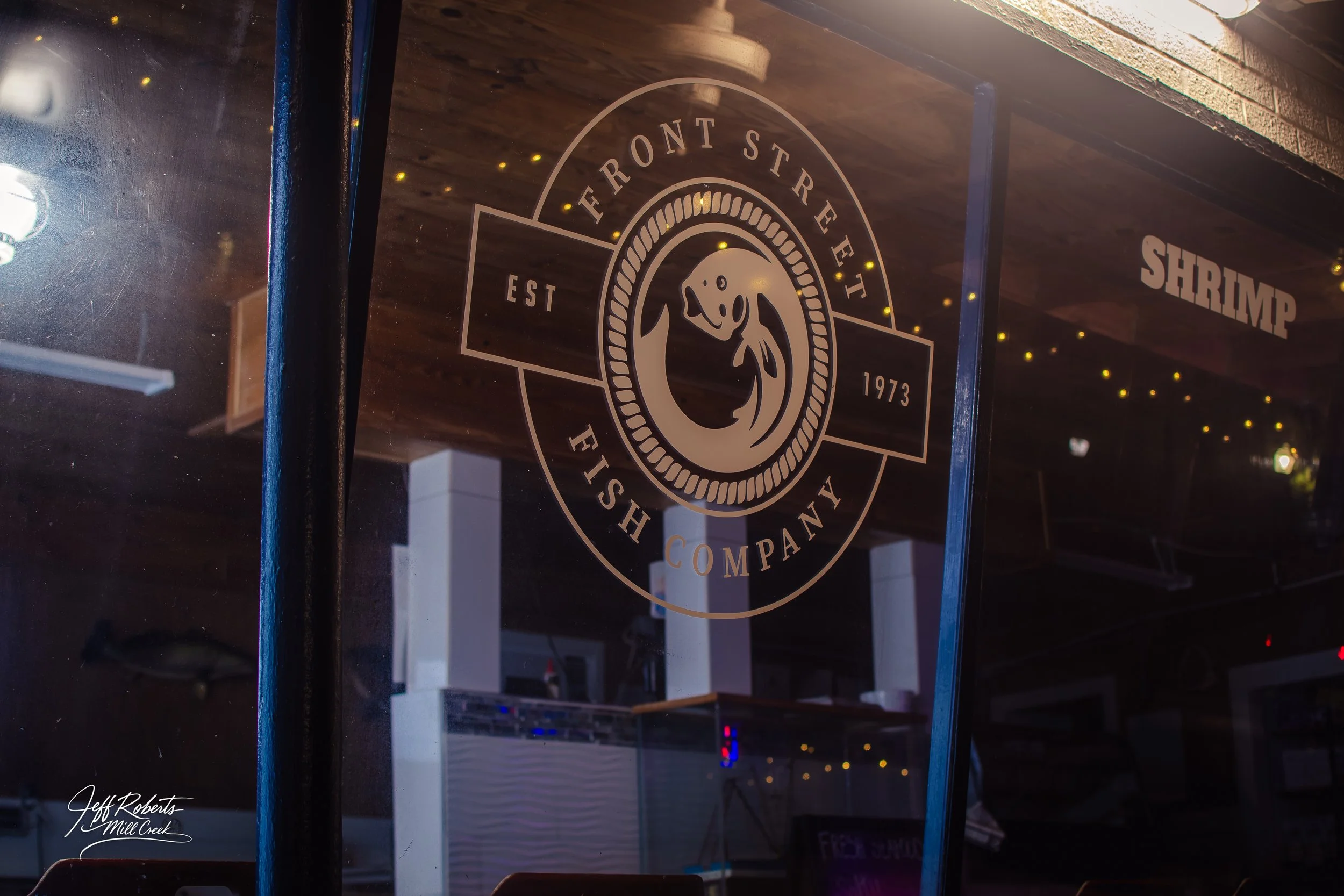 Glass window of a fish restaurant with the logo of Front Street Fish Company, showing a fish illustration and the text 'Est 1973 Front Street Fish Company'.