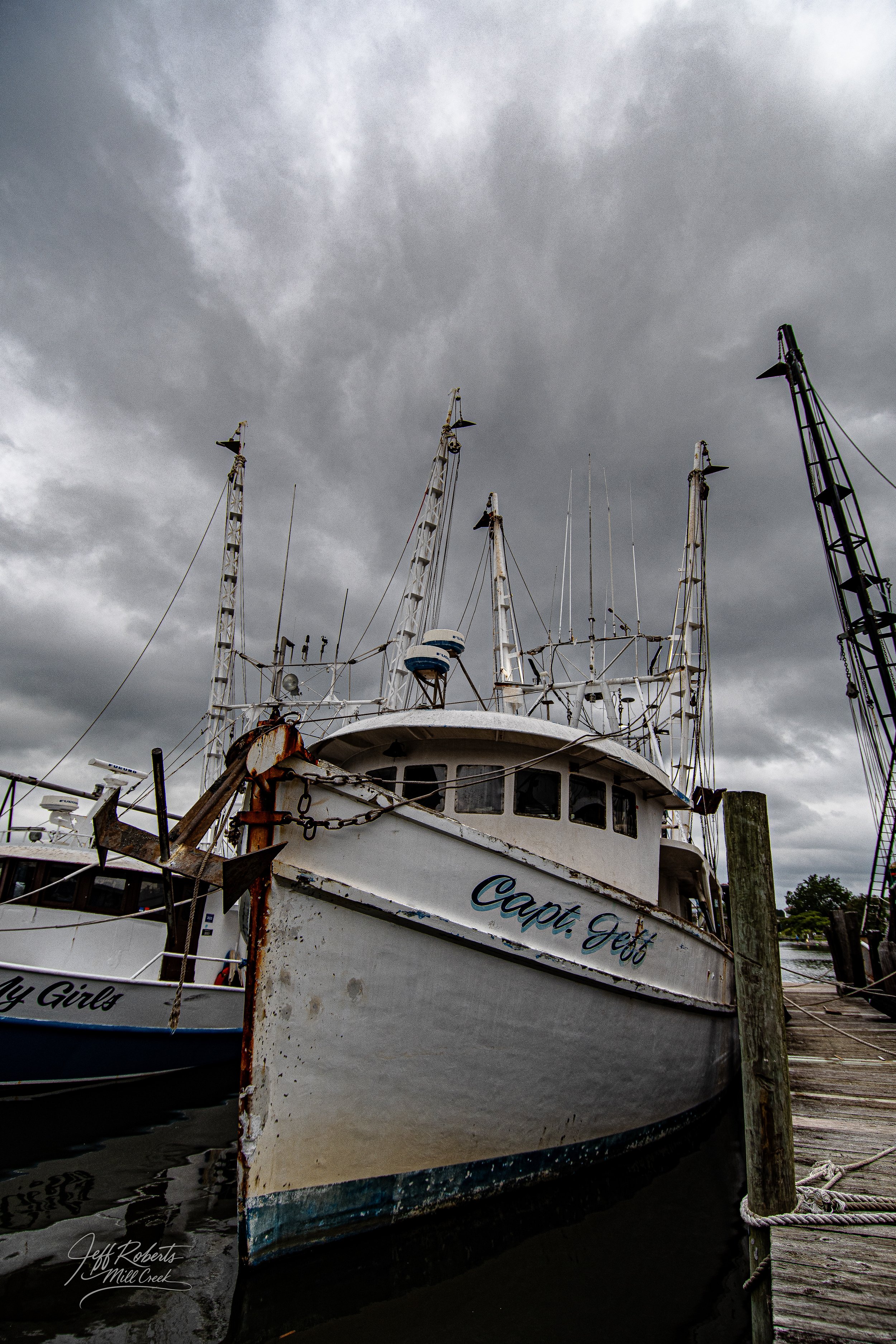 A large white boat named 'Capt. Jeff' docked at a pier on a cloudy day.