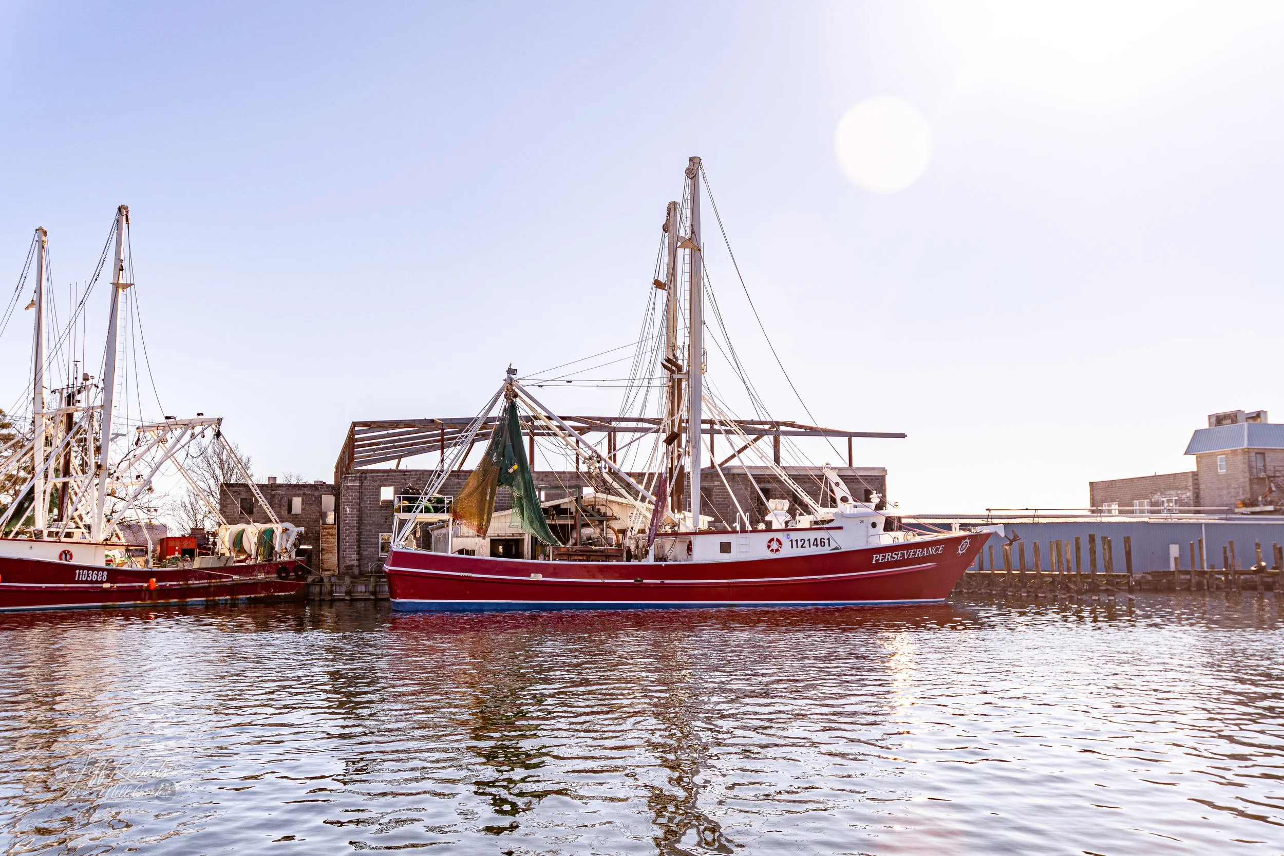 A red and white boat named PERSEVERANCE docked at a harbor during daytime with a clear sky and visible sunlight.