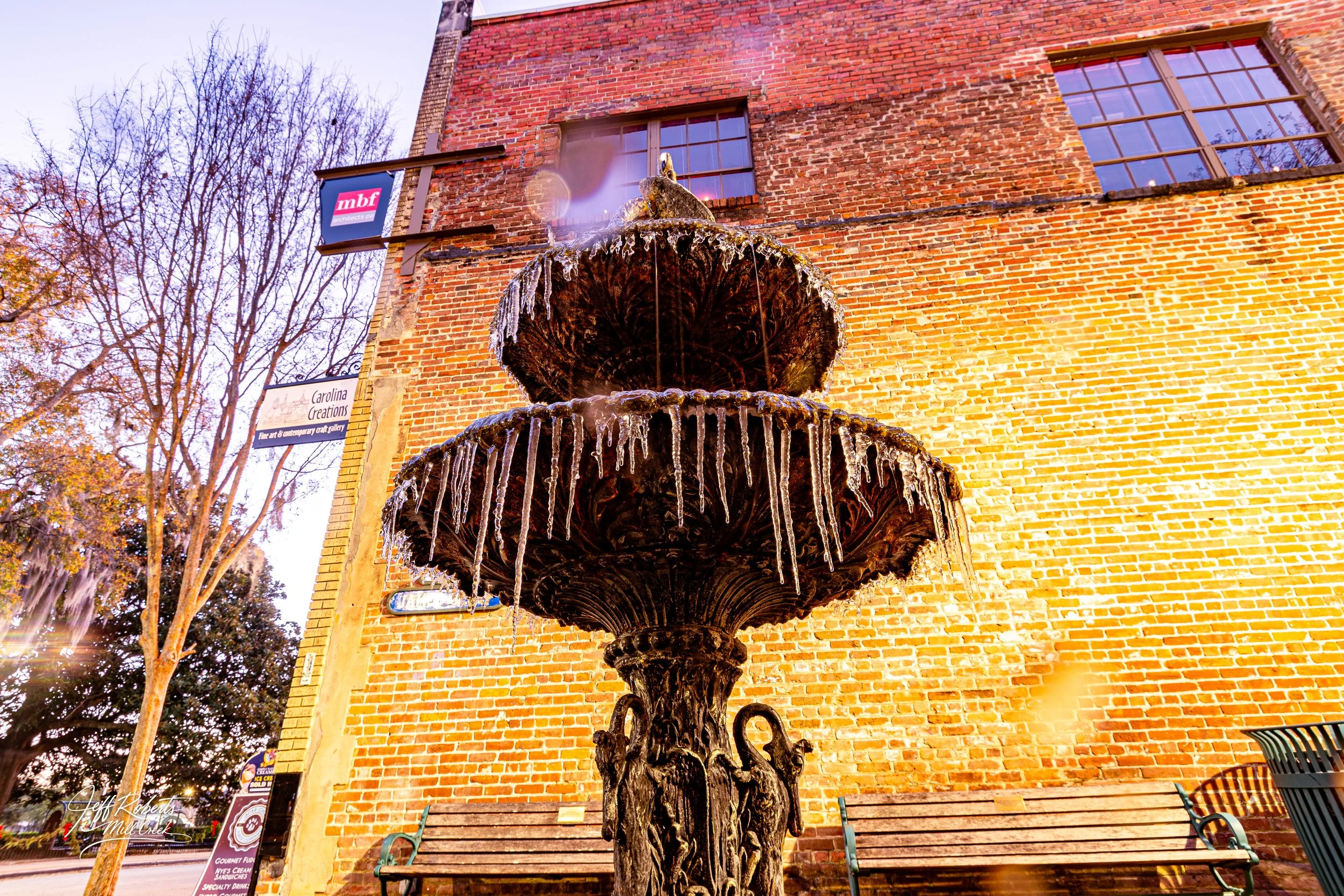 Iron fountain with water and icicles in front of a brick building during winter.