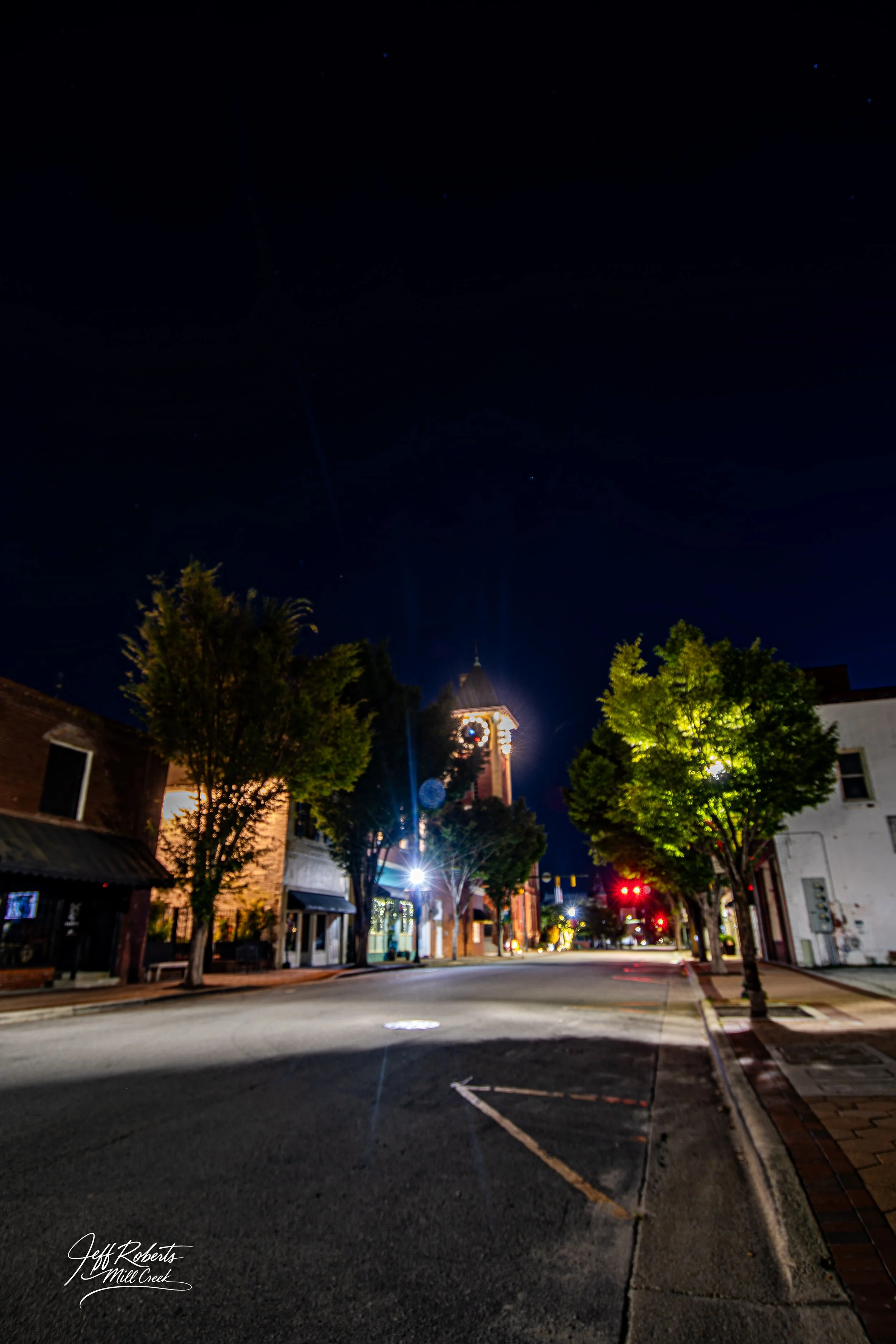 A quiet street scene at night with a clock tower and illuminated trees.