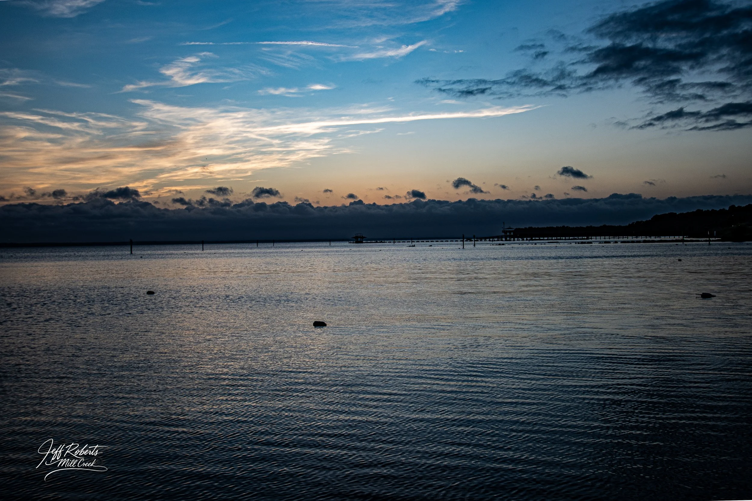 A scenic view of a lake at sunset with a cloudy sky and a distant pier extending into the water
