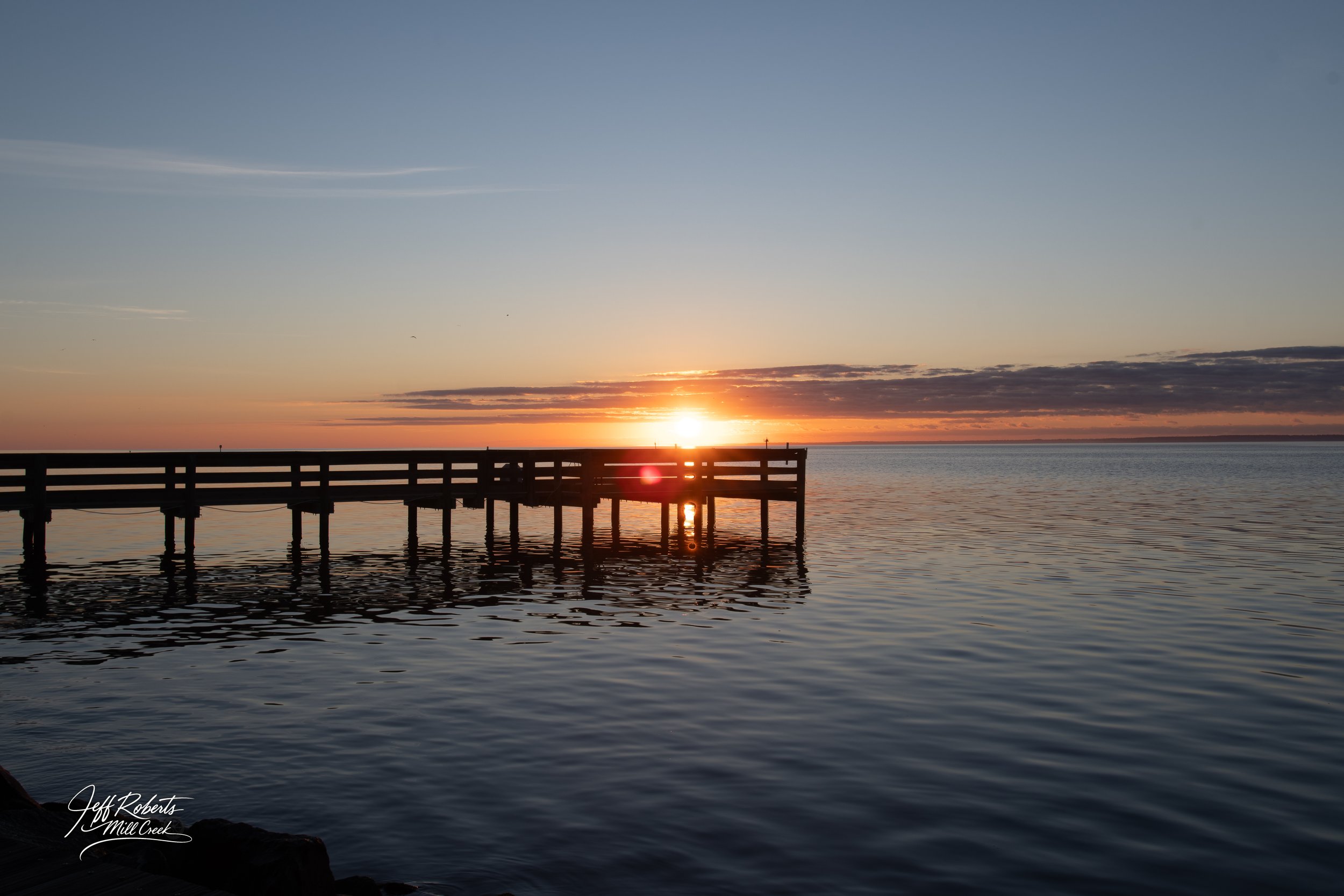 Sunset over a body of water with a wooden dock extending out into the water.