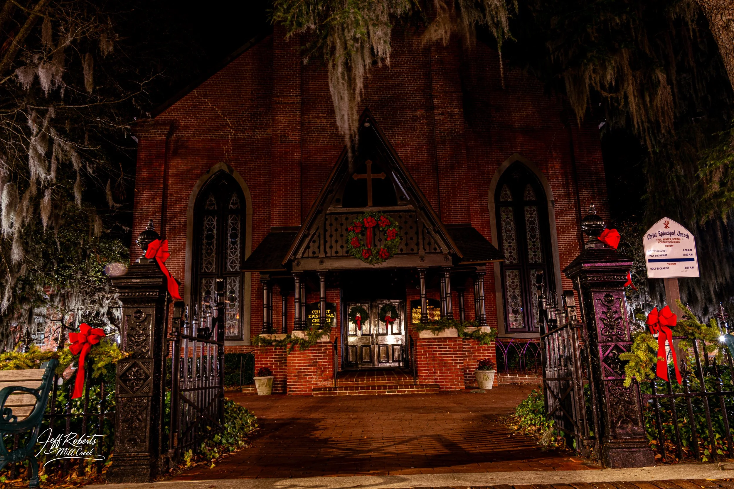 Night view of a brick church decorated for Christmas, with wreaths and red bows on the entrance gate and building.