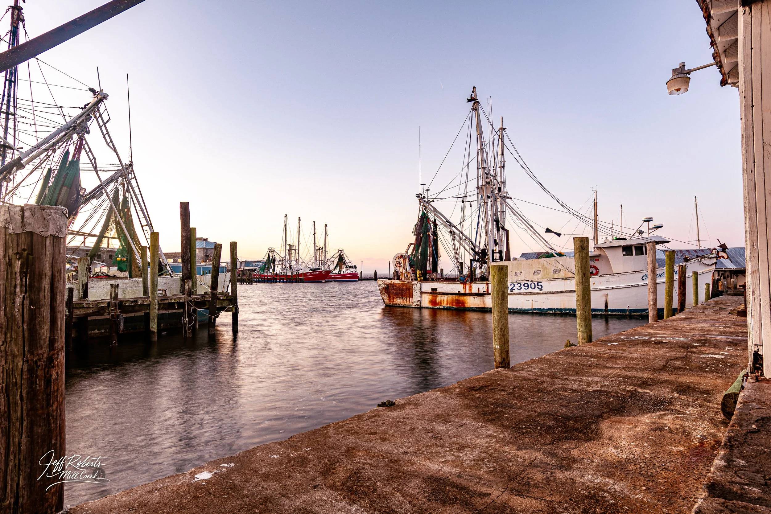 Boats docked along a pier at sunset with calm water and a clear sky.