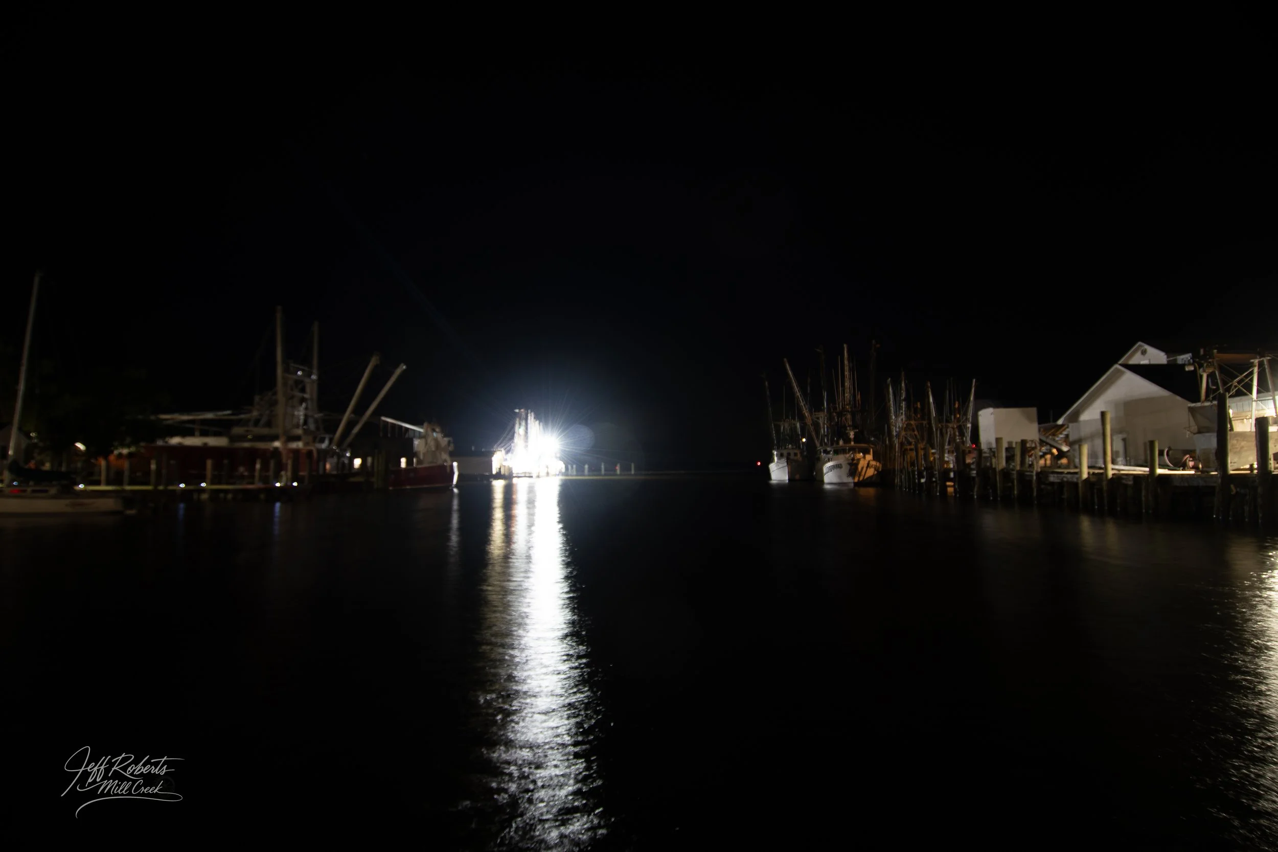 Nighttime view of boats docked at a marina with bright light reflecting on the water.