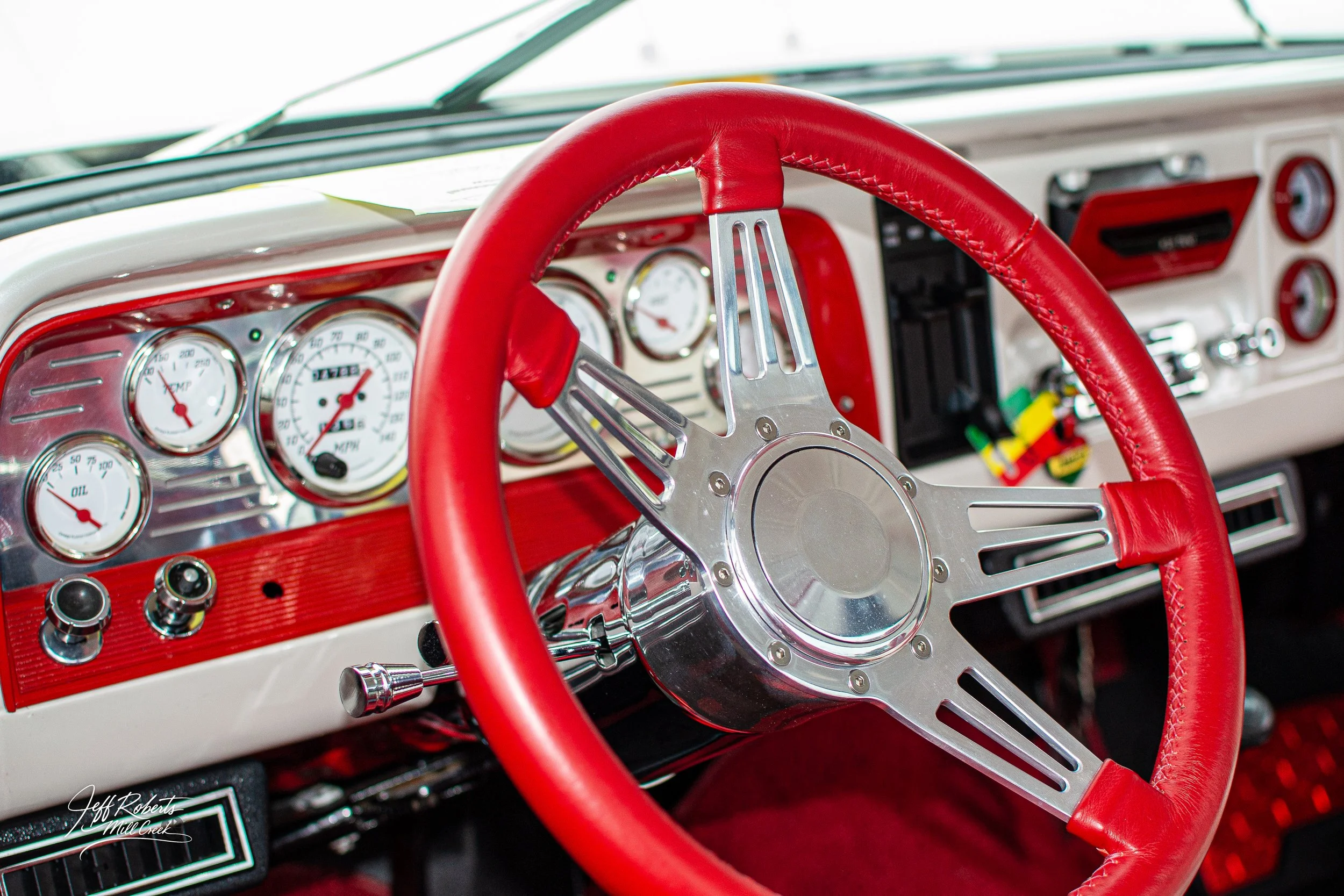 Close-up of a vintage car dashboard with a red leather steering wheel, white gauges, and chrome accents
