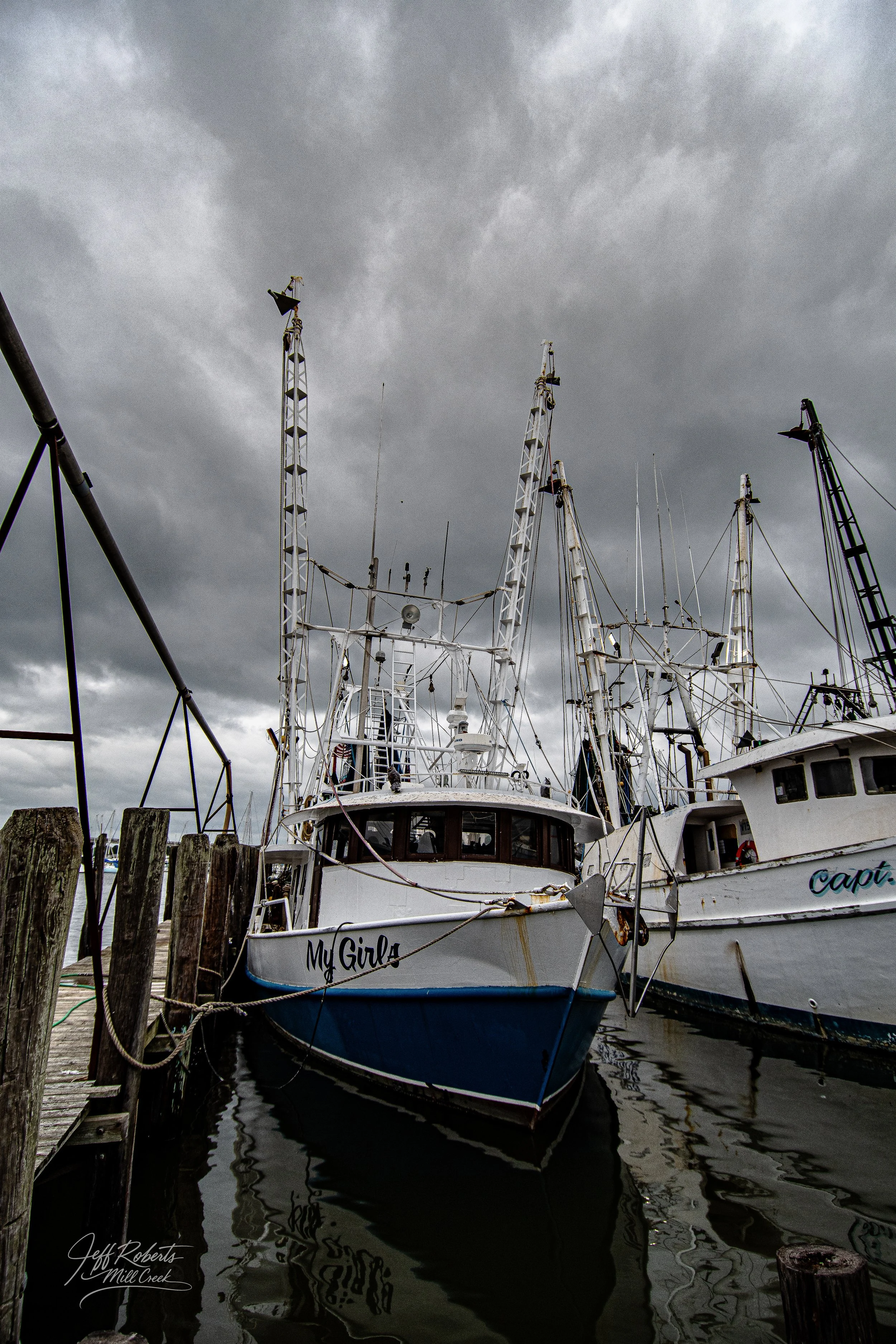 Several fishing boats docked at a pier on a cloudy day, with the boat named 'My Girls' visible in the foreground.