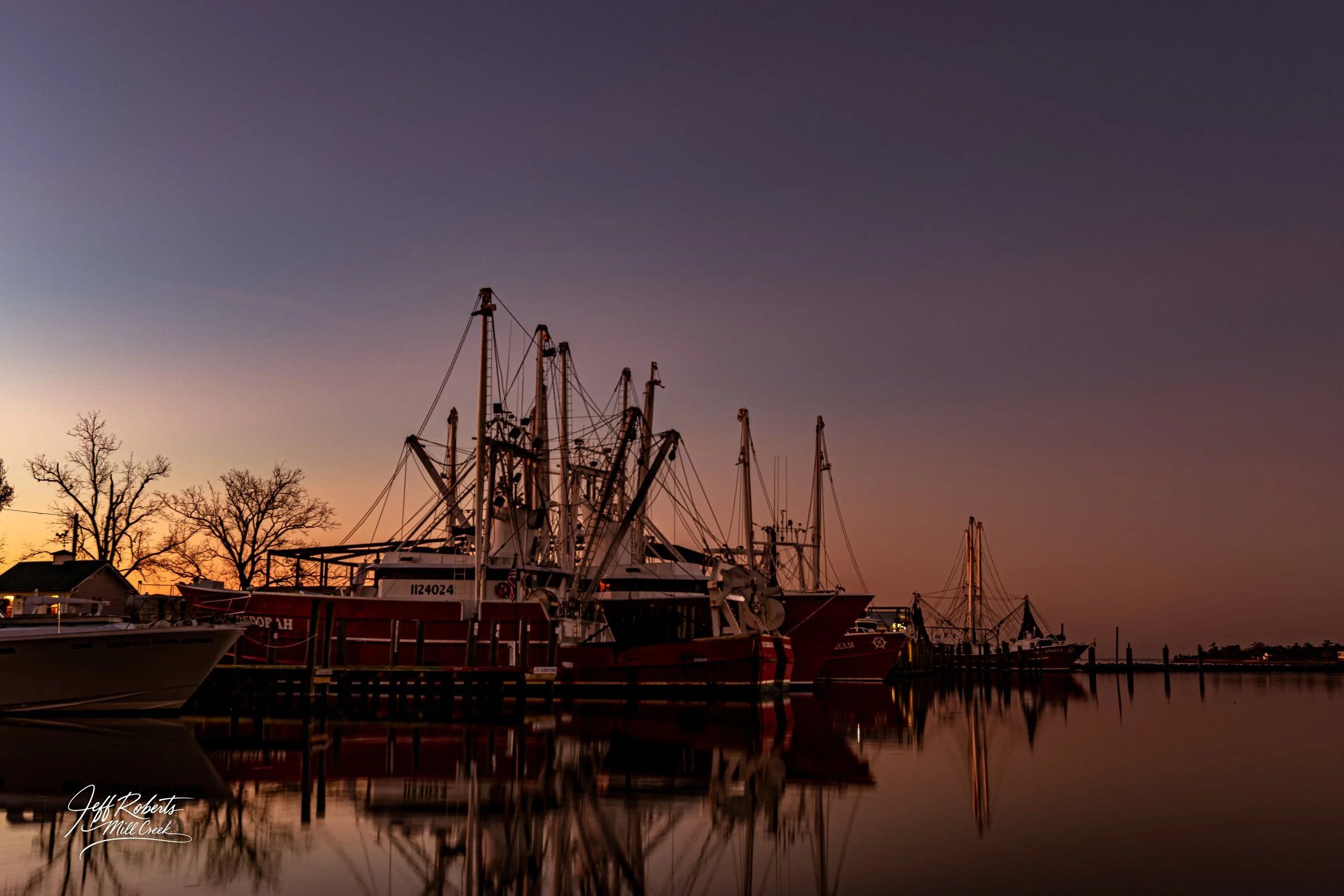 Boats docked at a marina during sunset with a calm water reflection and a gradient sky