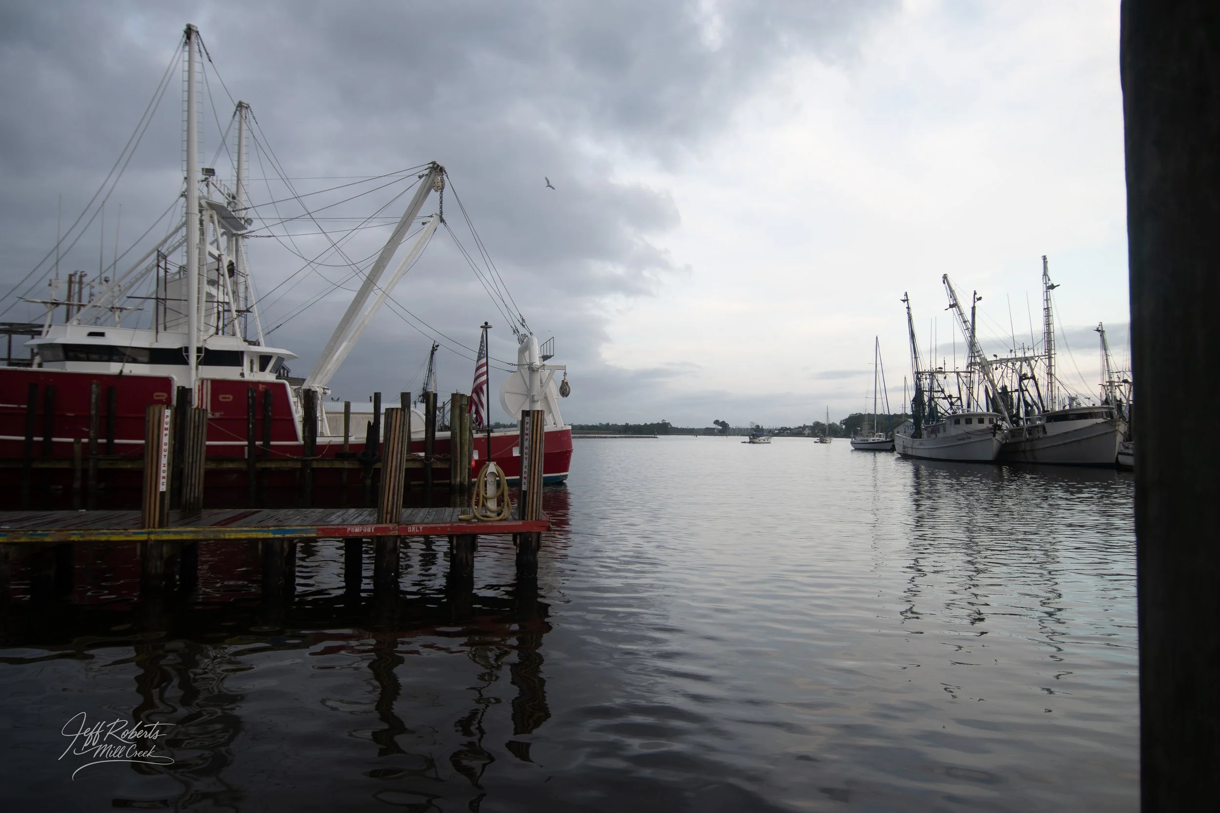 A harbor with multiple boats docked, including a large red and white boat on the left and several fishing boats on the right, under a cloudy sky.