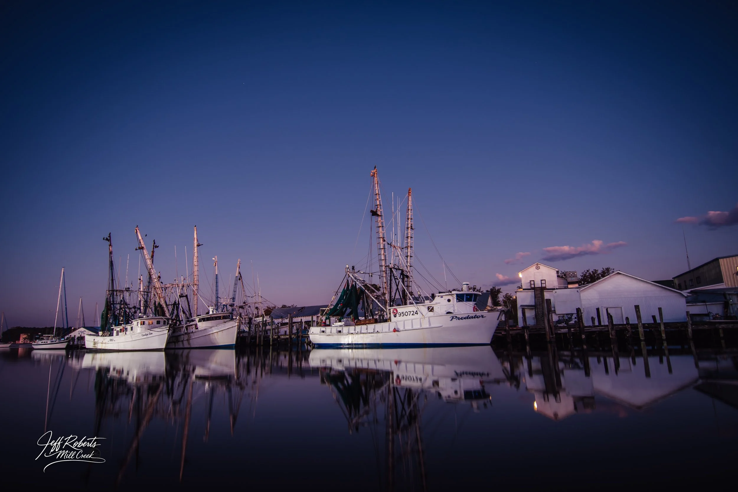 Boats docked at a calm marina during twilight with clear sky and reflected water