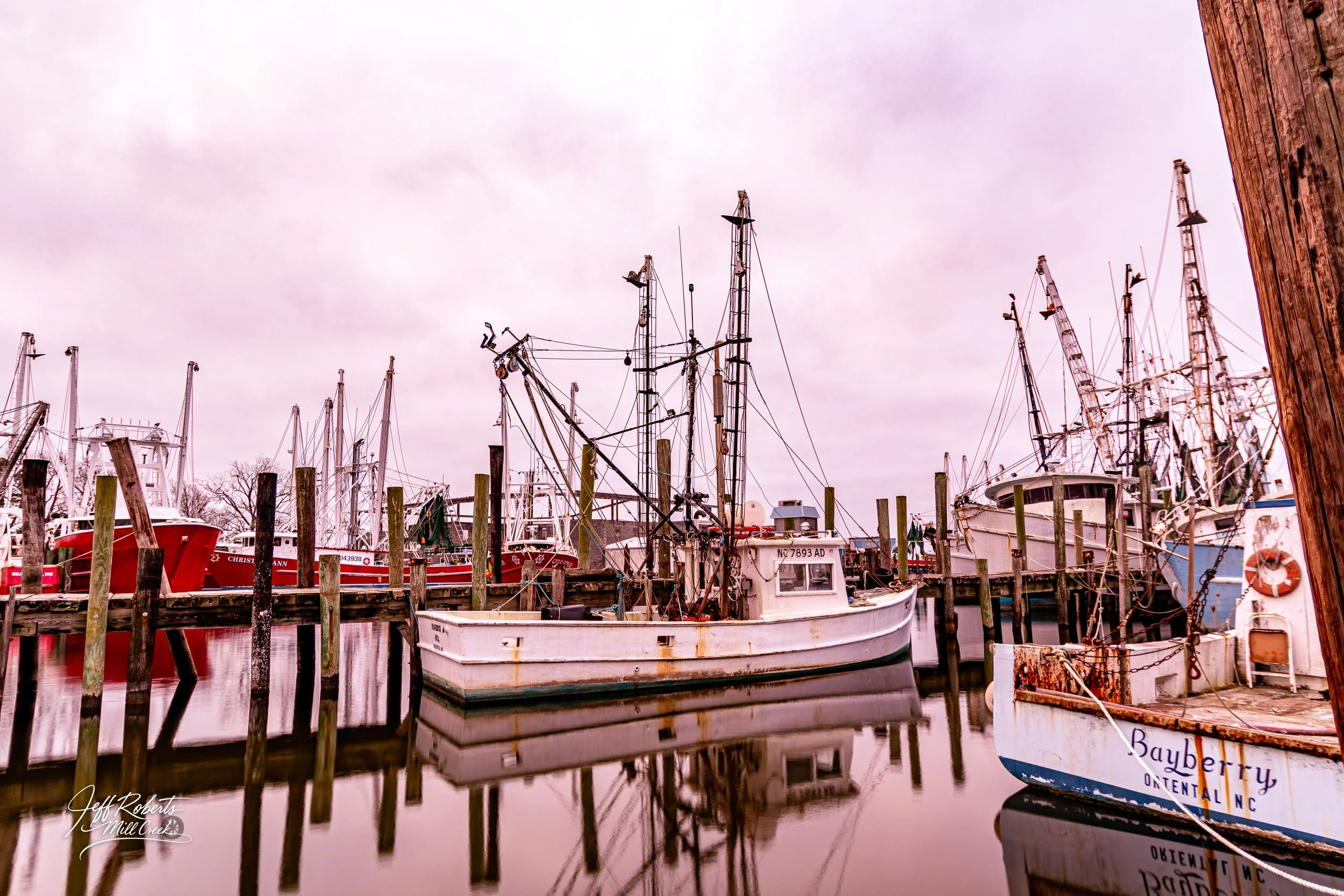 Boats docked at a marina with reflections on calm water and overcast sky