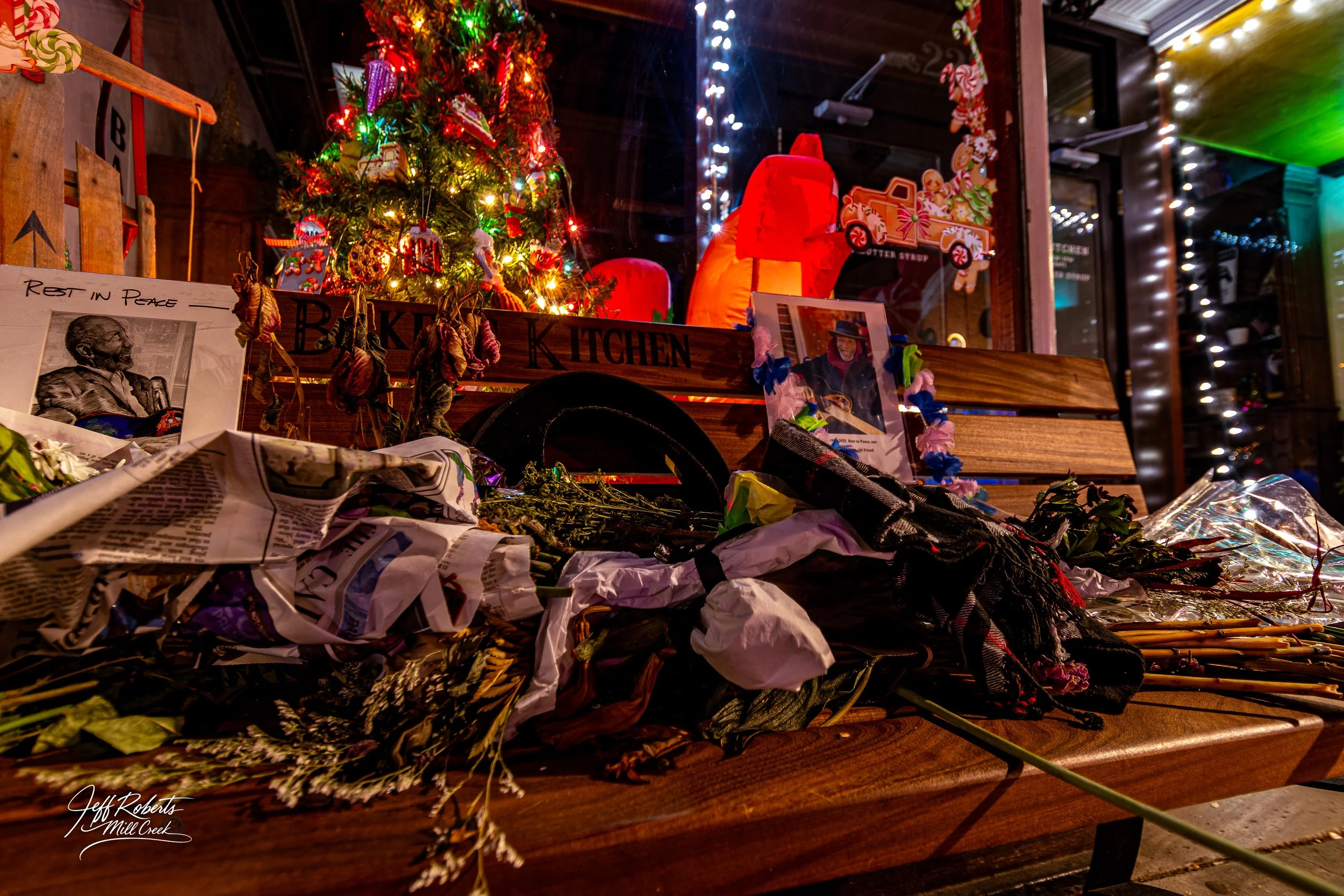 Memorial with flowers, photographs, and Christmas decorations in front of a Christmas tree, showing a tribute to a person who passed away.