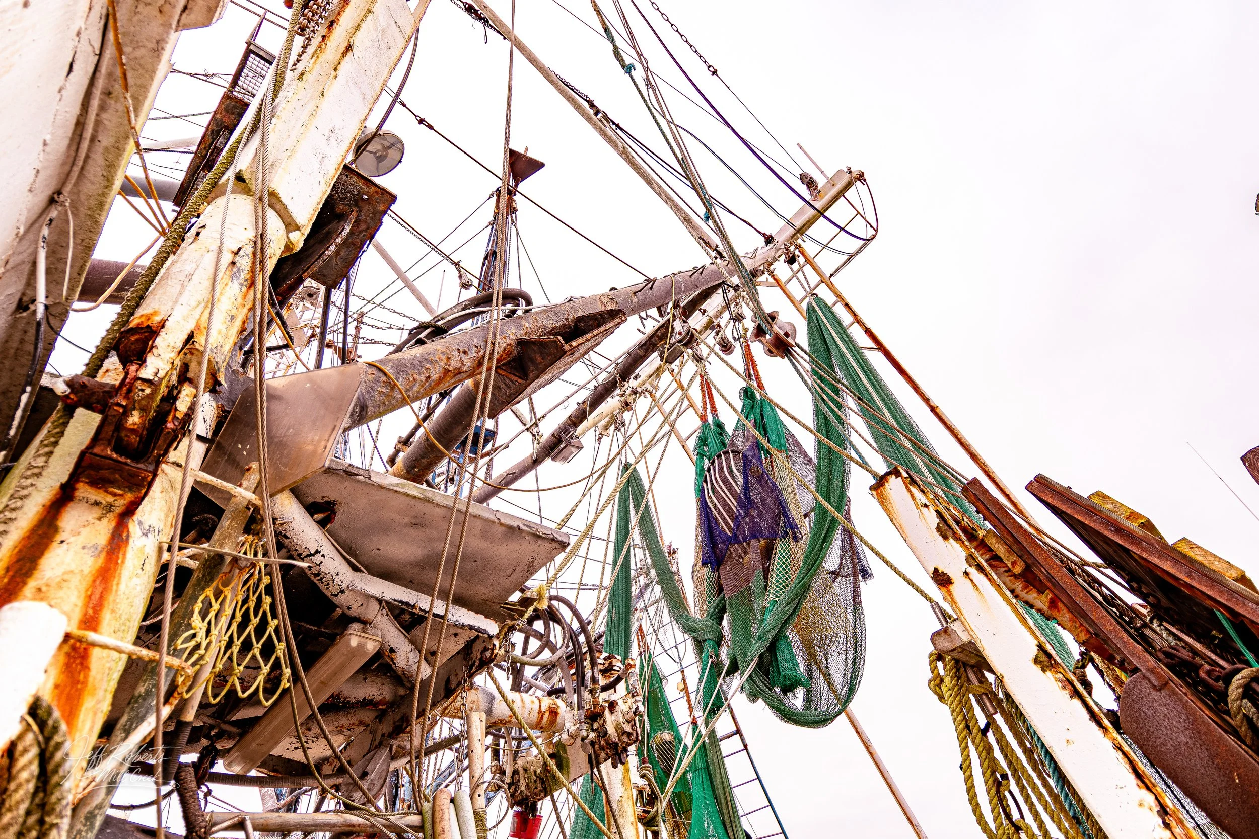 Close-up view of the rusted masts, rigging, and nets of an old, abandoned sailing ship against a cloudy sky.