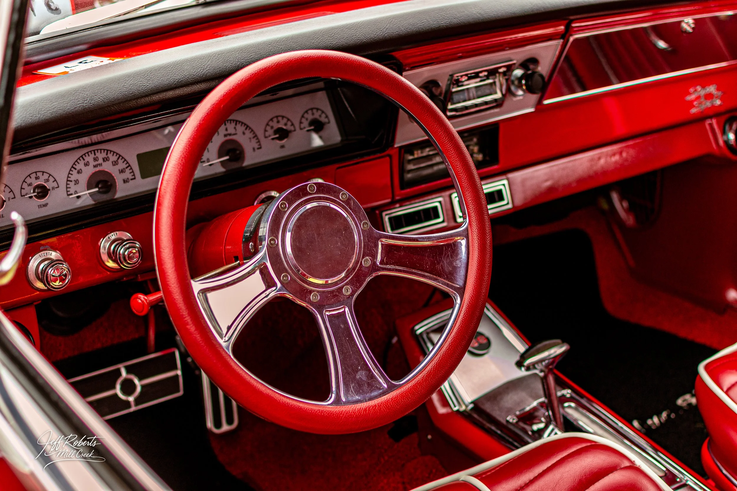 Interior of a vintage red car showing a red steering wheel with a chrome center, white dashboard with gauges, and red interior accents.