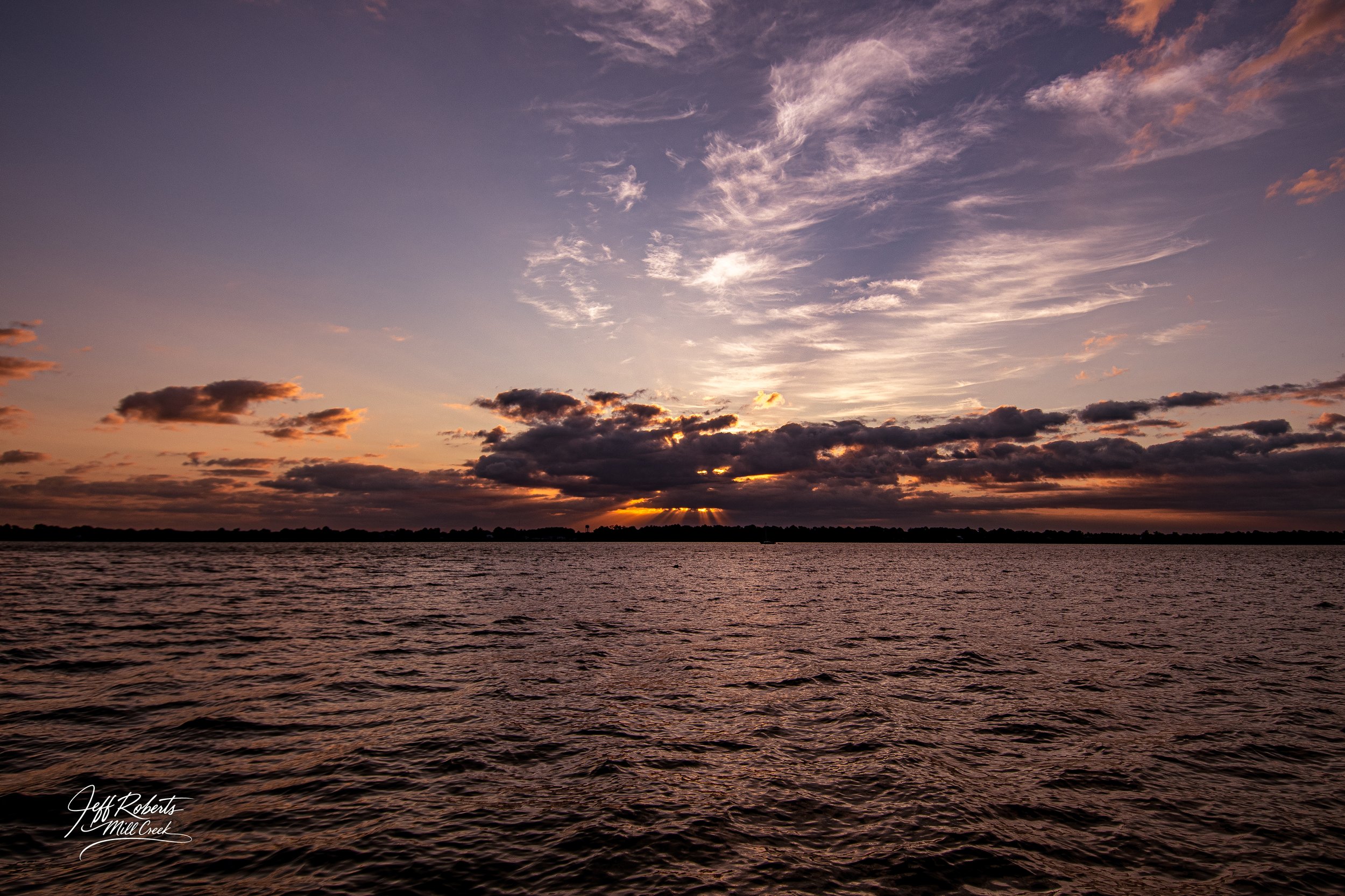 Sunset over a body of water with clouds in the sky.