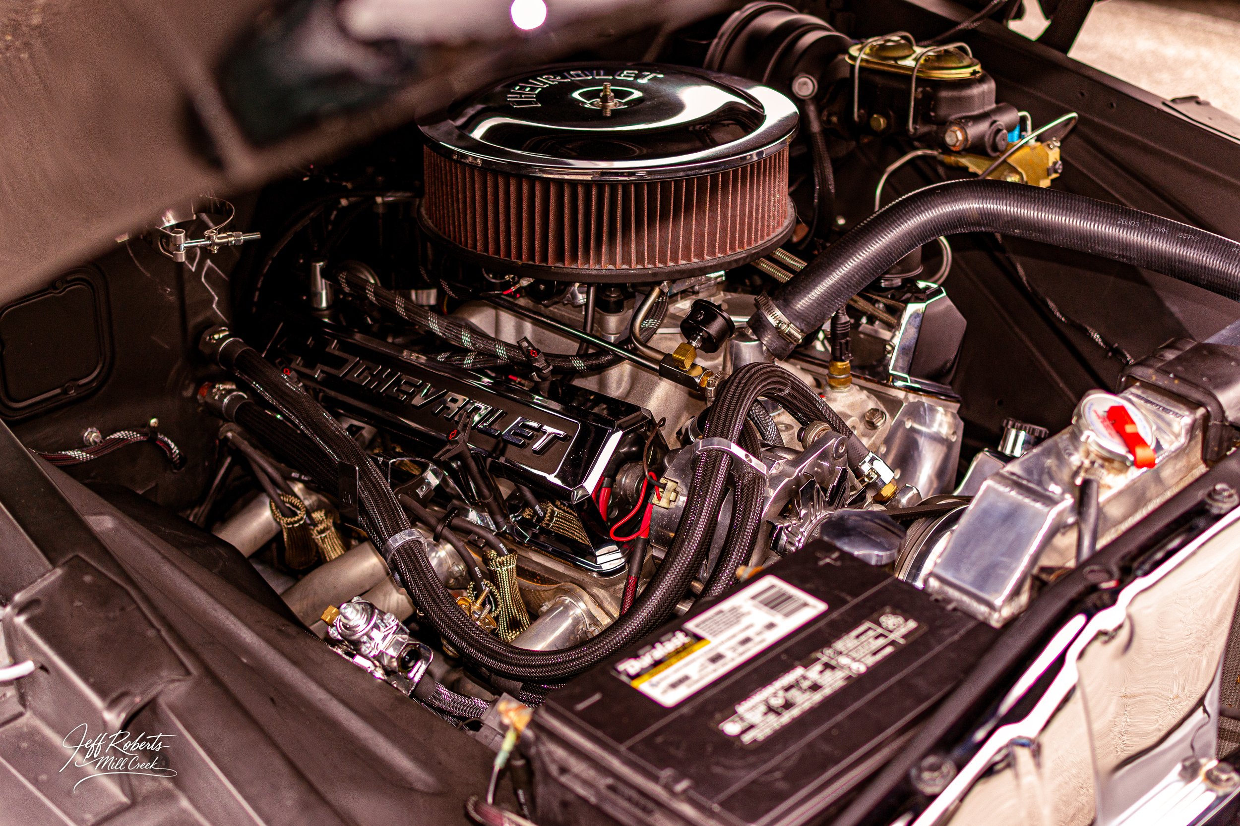 Close-up view of a Chevrolet engine inside a car's engine bay, featuring a large air filter, hoses, and metallic components.