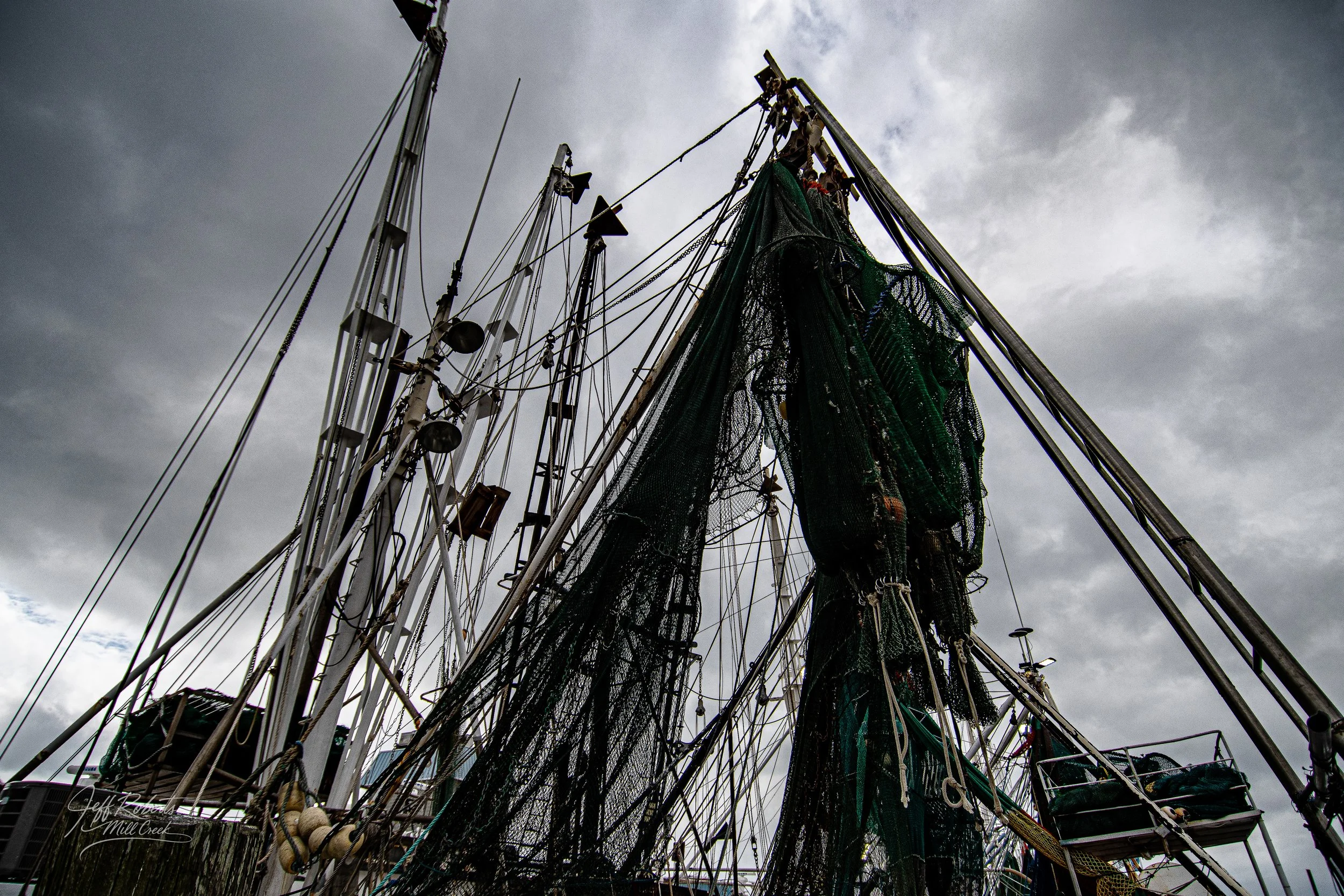 View of fishing boats with nets and rigging against a cloudy sky.