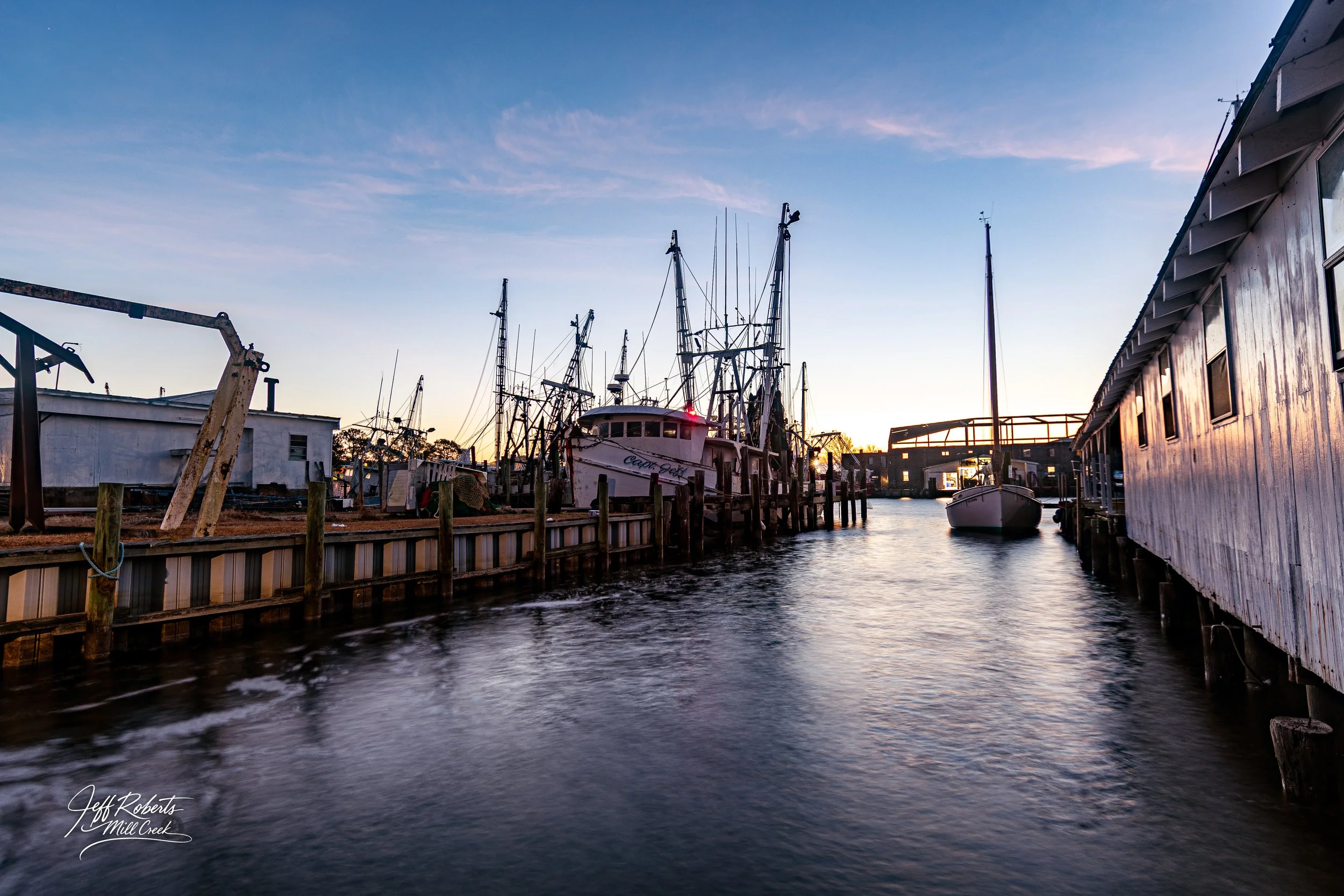 Boats docked at a marina during sunset with calm water and clear sky.