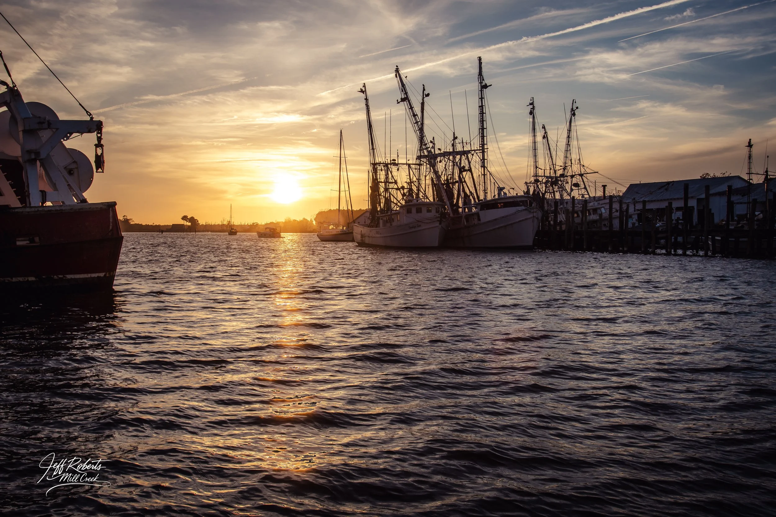 Boats docked at a marina during sunset with a partly cloudy sky and calm water.