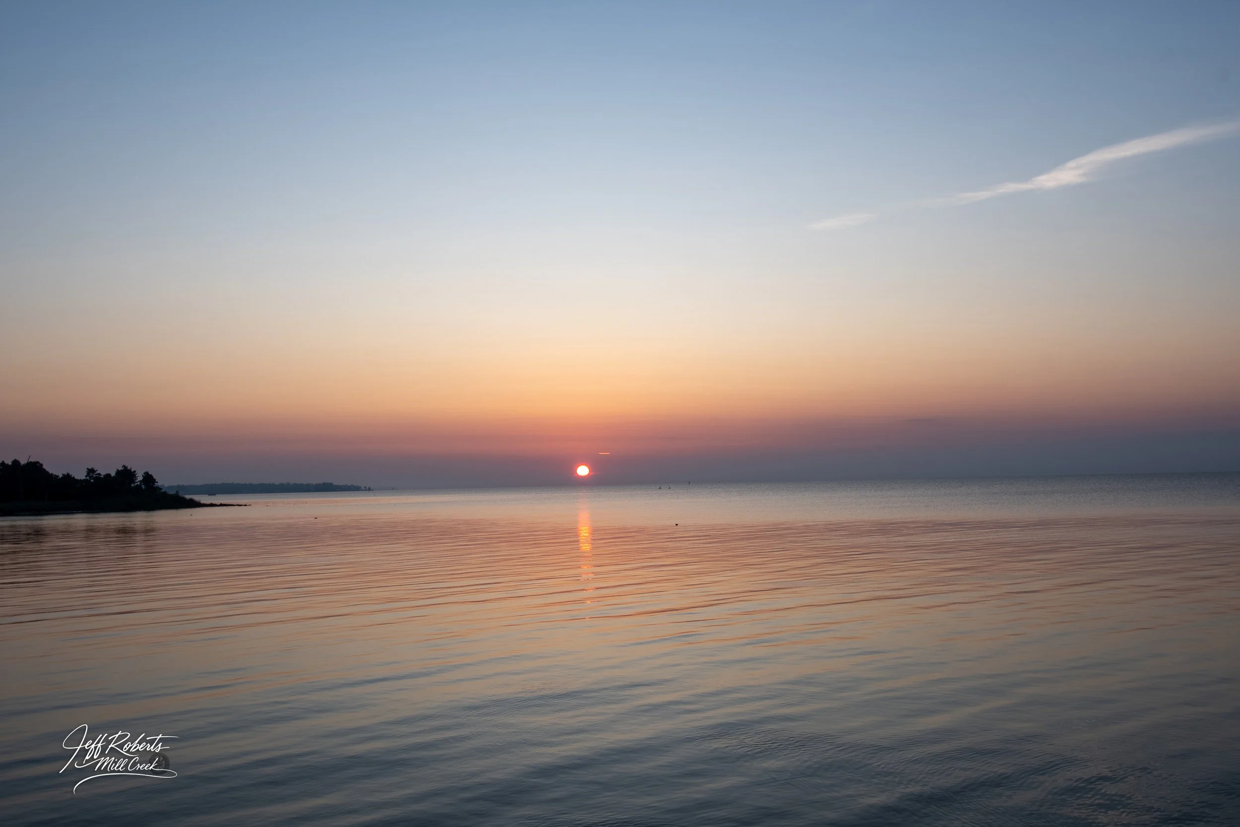 Sunset over calm water with a distant shoreline and a clear sky