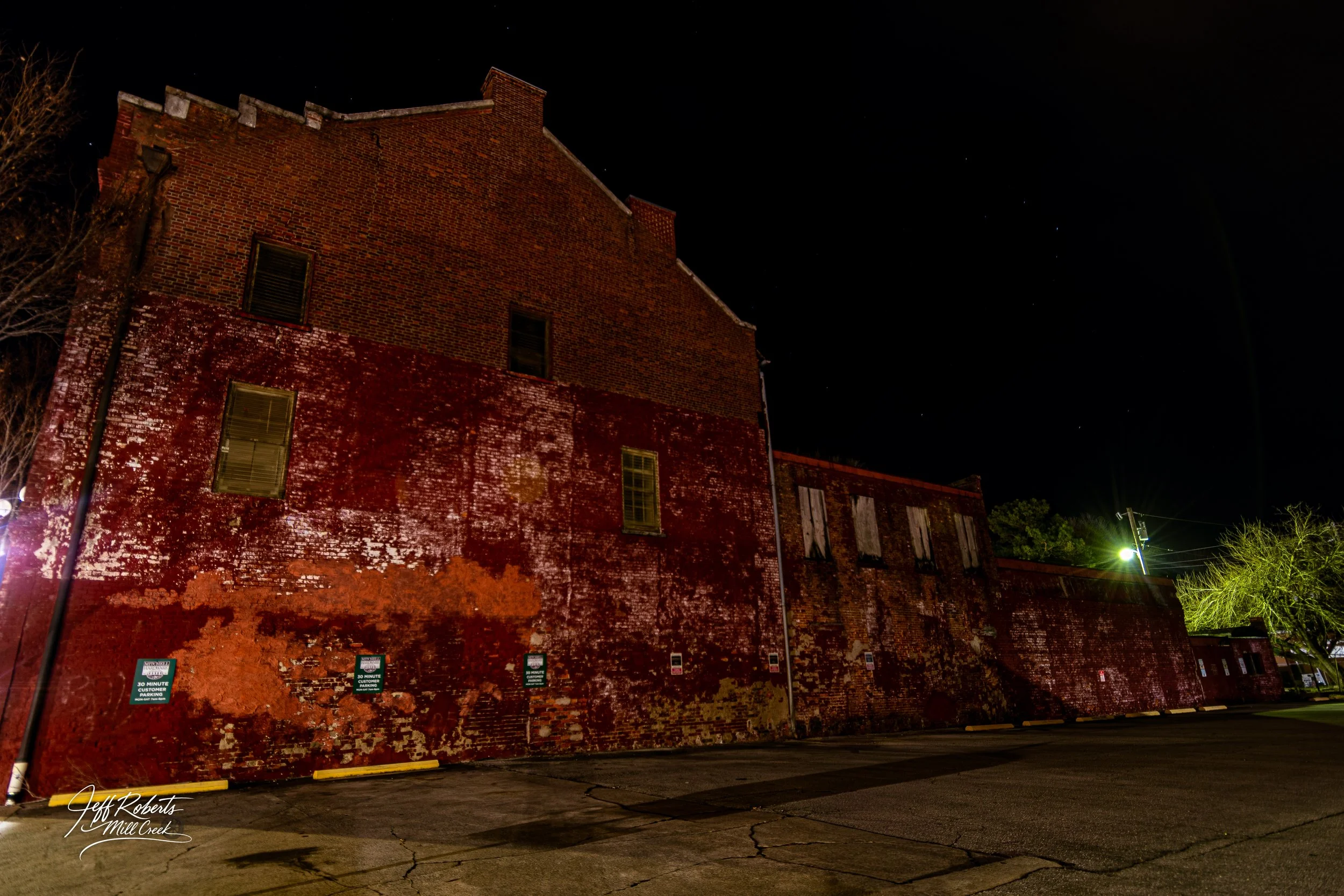 Night view of an old brick building with weathered red and brown walls, boarded-up windows, and bright streetlights illuminating the scene.
