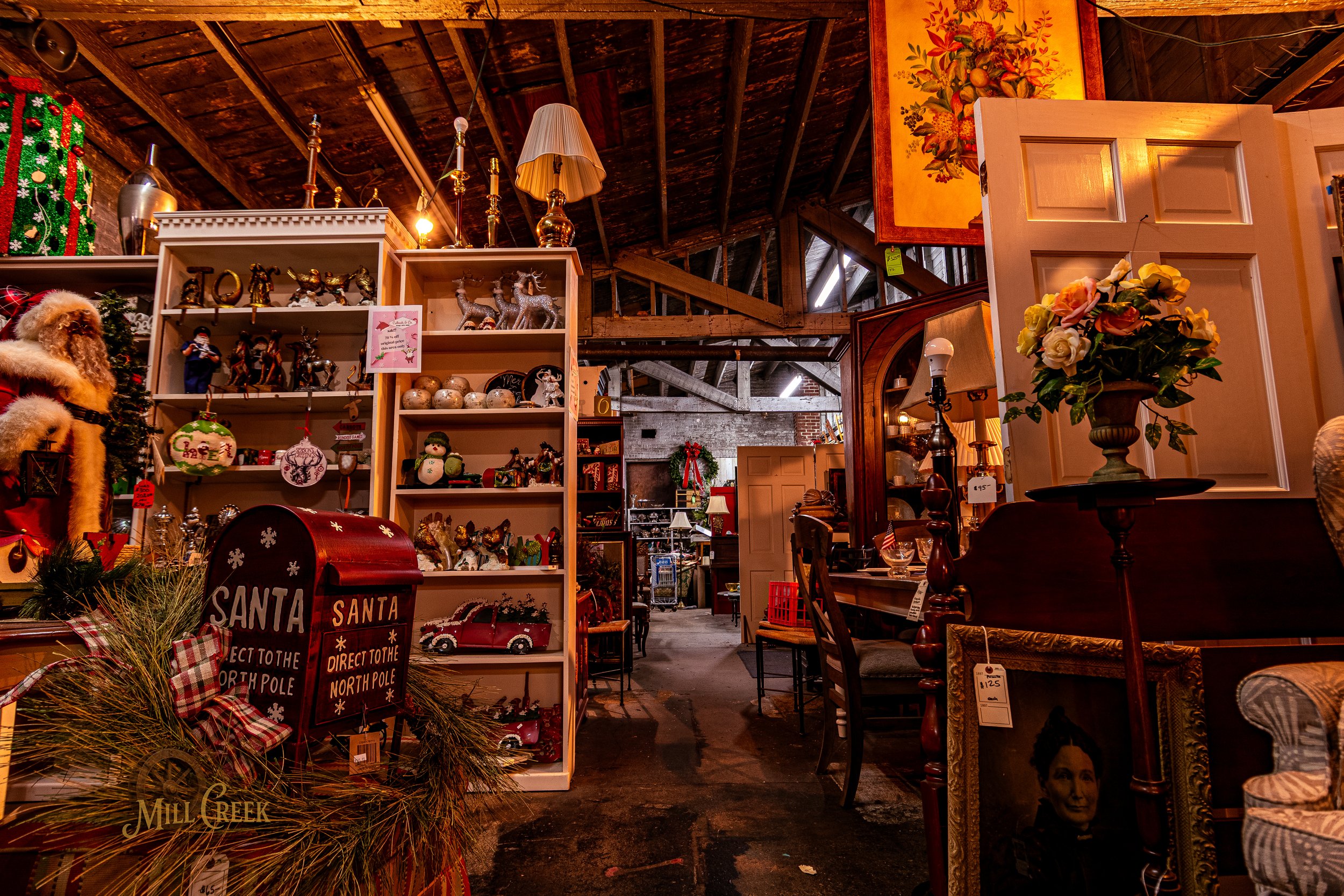 Interior of a thrift store decorated for Christmas with various holiday items, ornaments, furniture, and a red mailbox for Santa in the foreground.