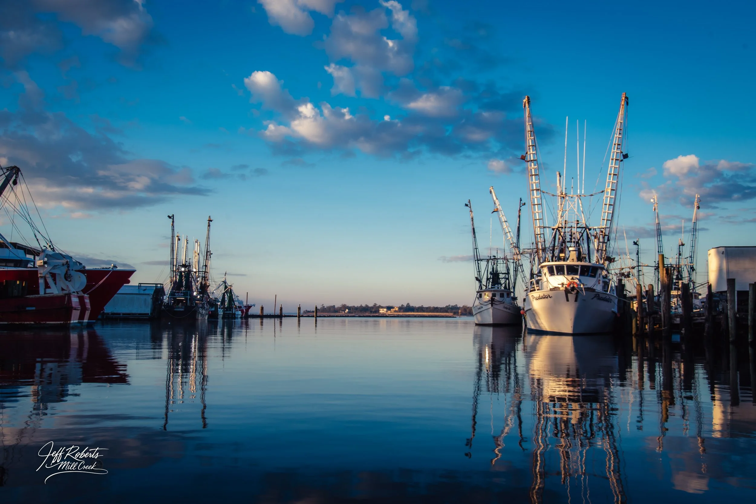 Boats docked at a marina during sunset, with calm water and a partly cloudy sky.