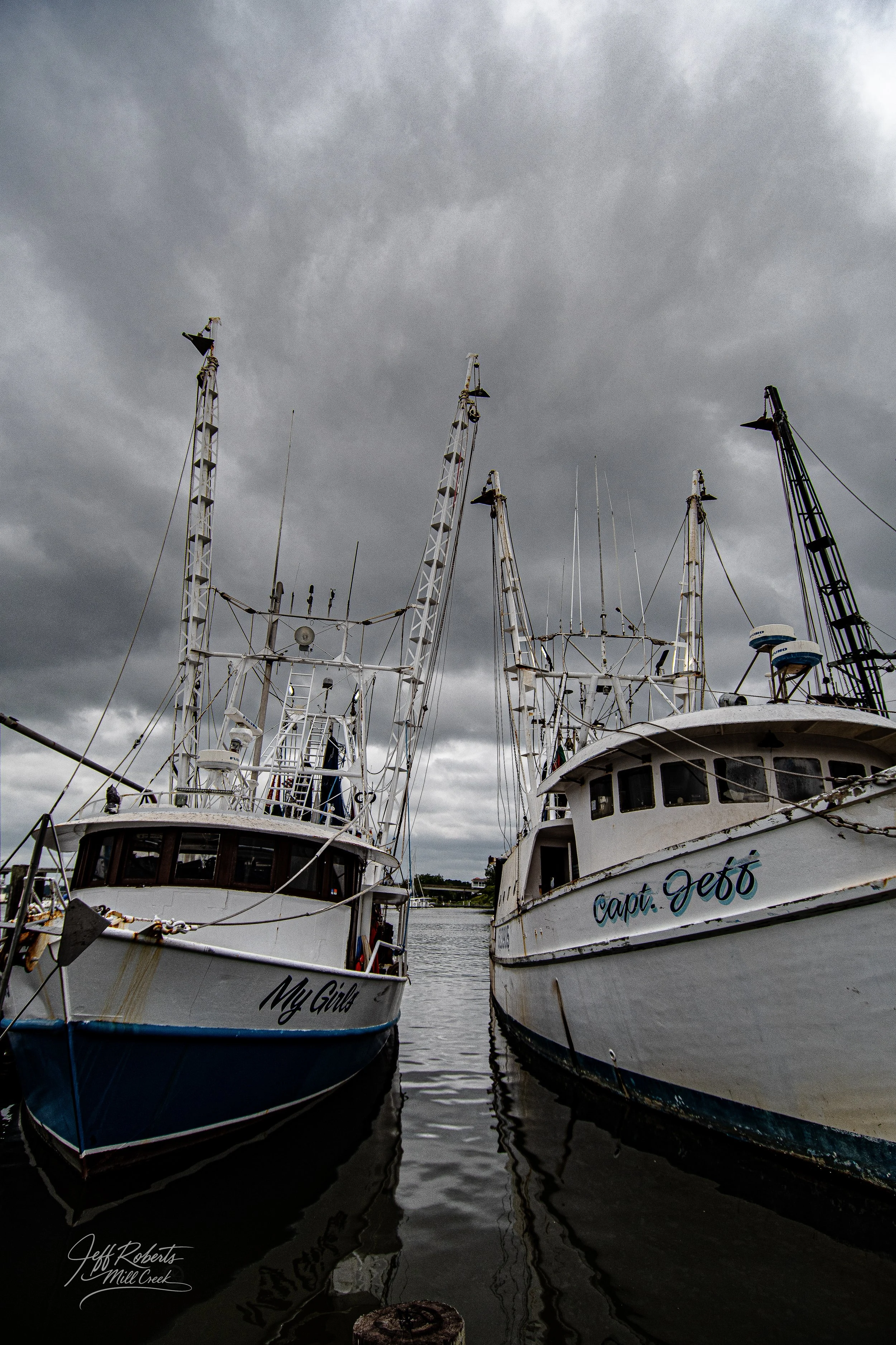 Two boats docked side by side on a cloudy day at a marina.