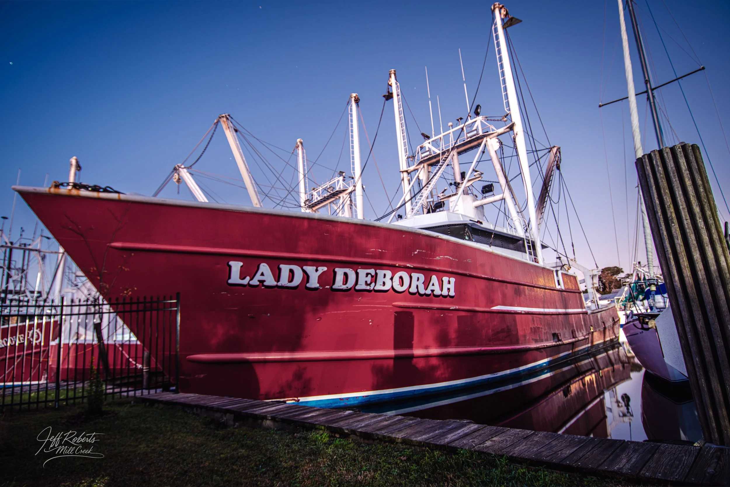 A large red fishing boat named Lady Deborah docked at a marina with other boats, under a clear blue sky.