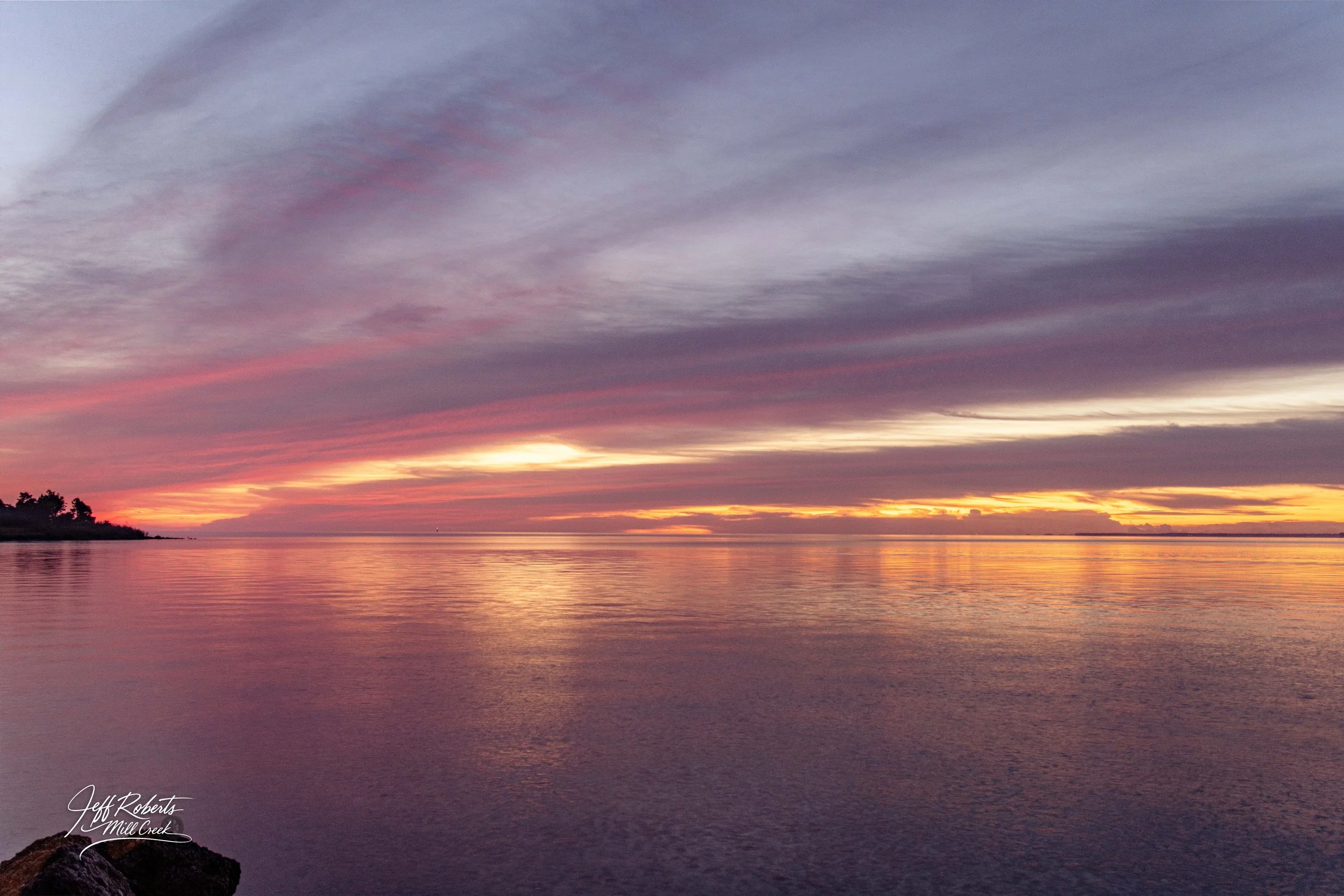 Sunset over a calm body of water with purple, pink, and orange clouds in the sky.
