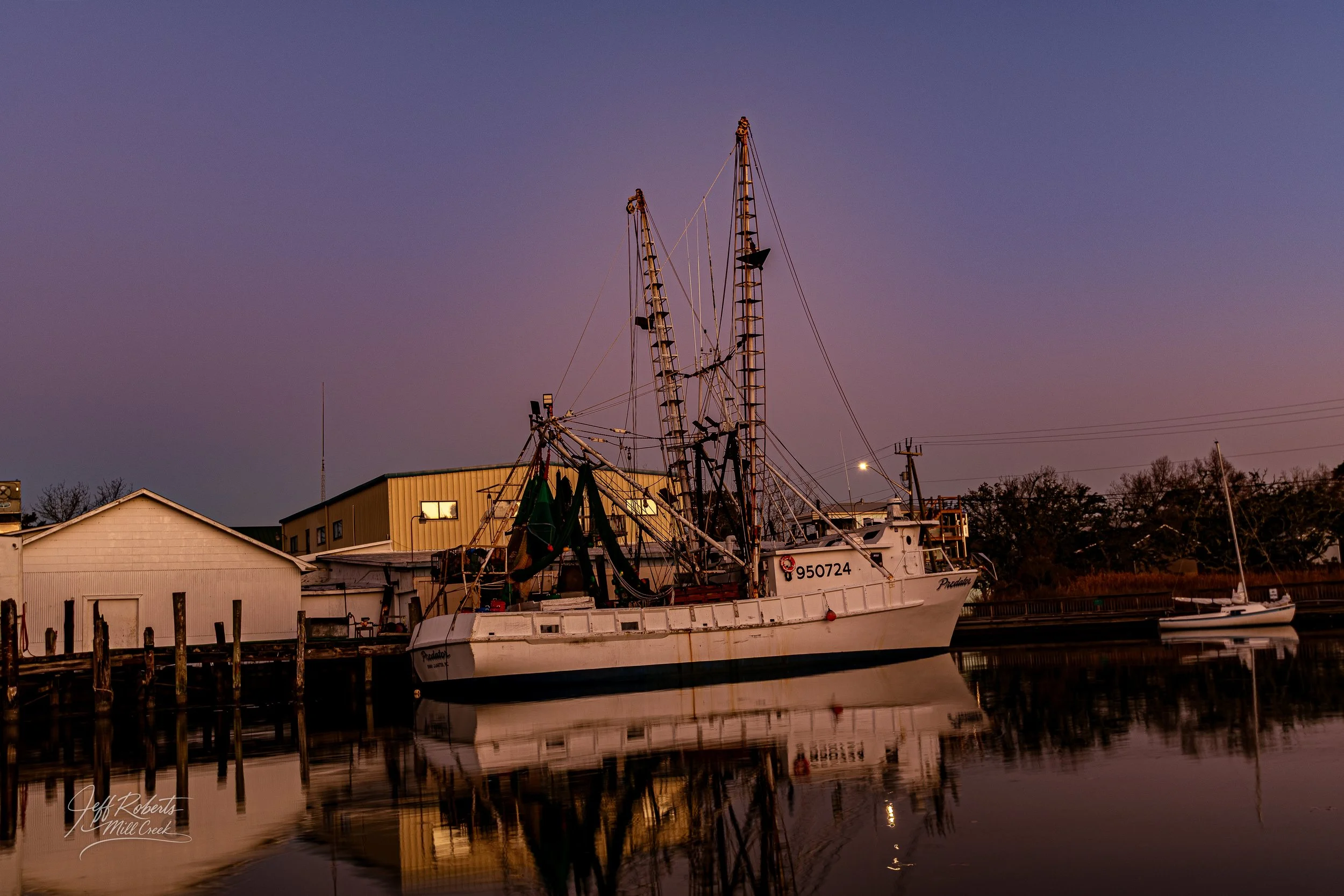 A fishing boat named 'Preacher' docked at a marina during twilight, with calm water reflecting the boat and nearby buildings.