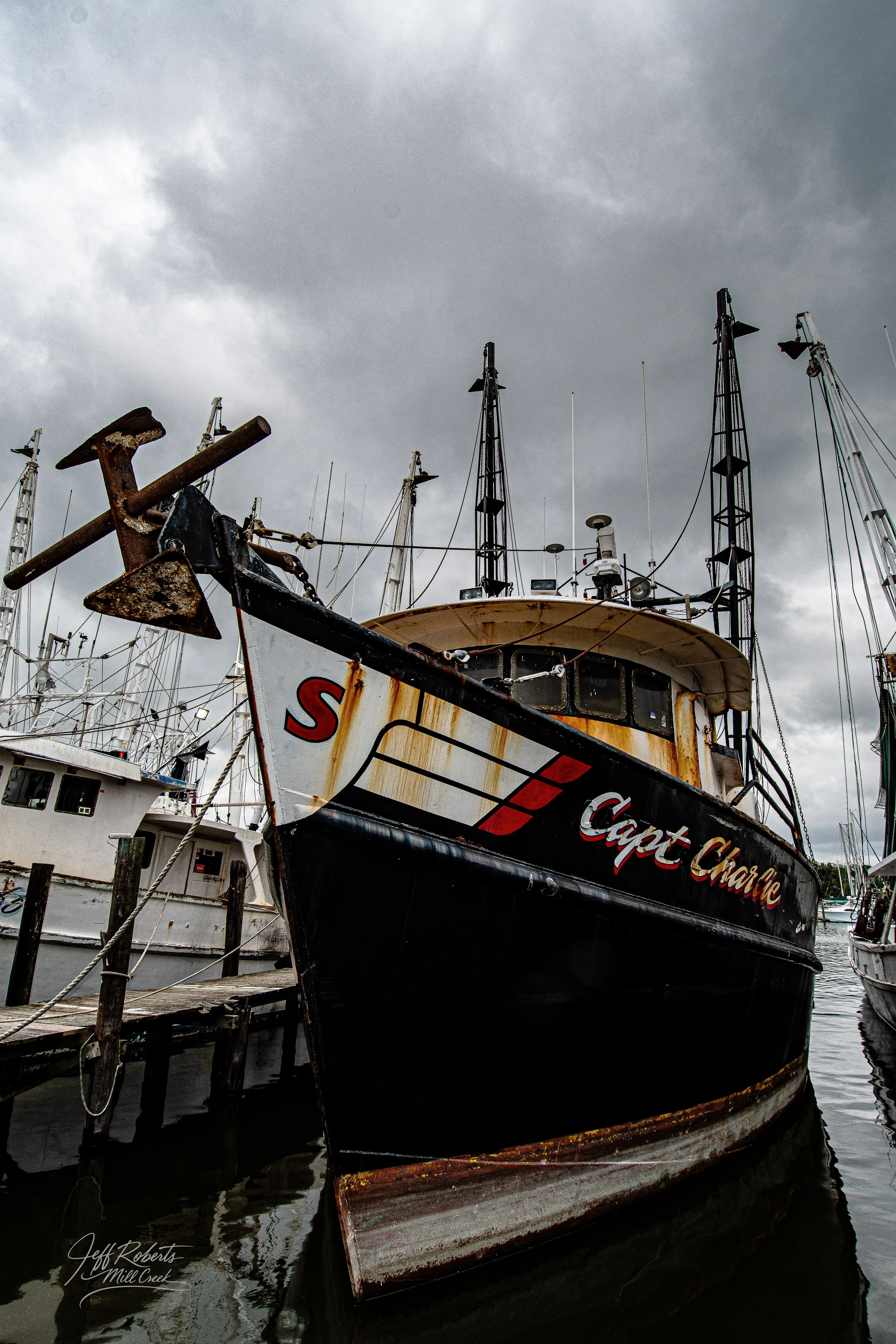 An old, rusty fishing boat named "Capt. Charlie" docked at a marina with other boats on a cloudy day.
