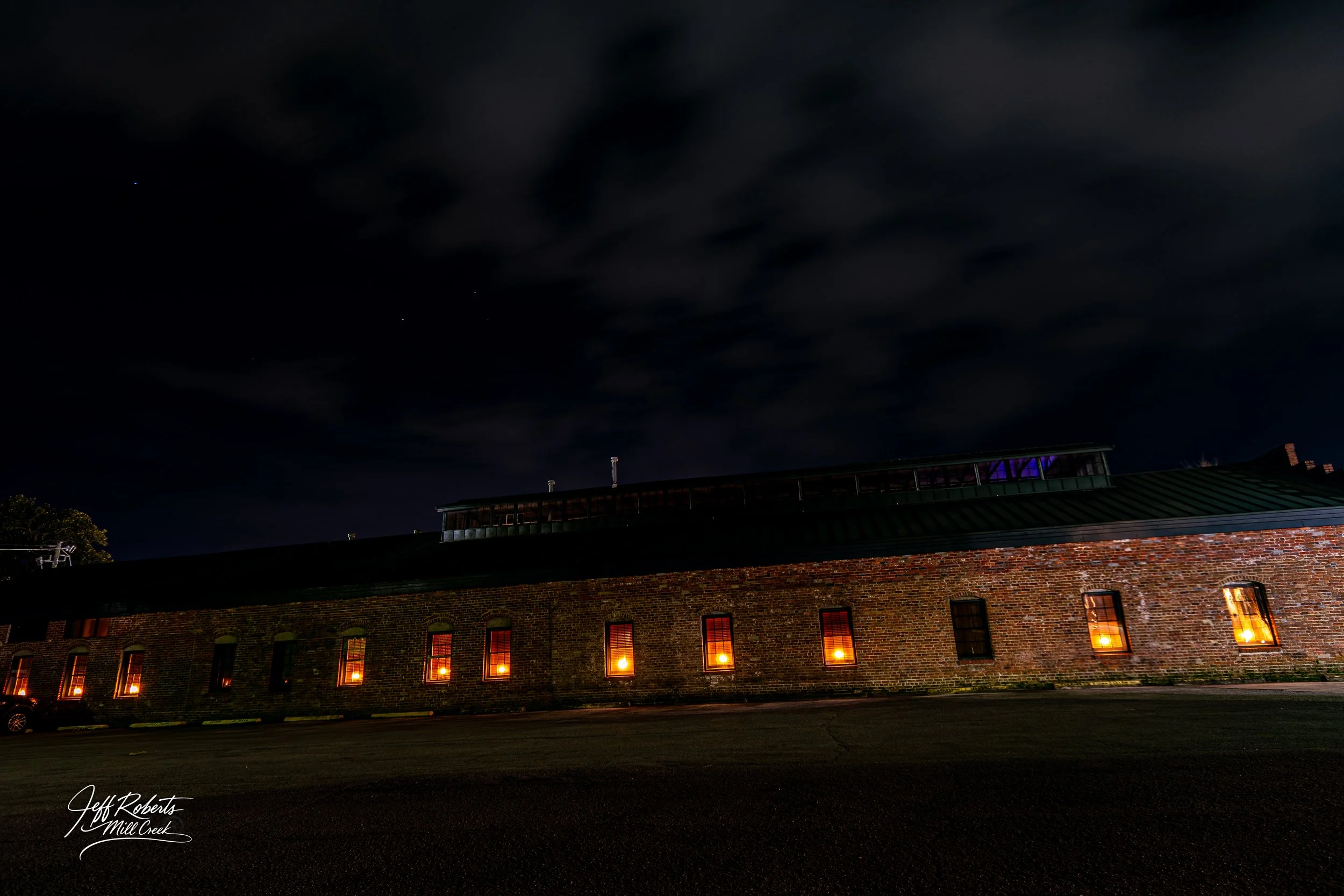 Nighttime view of a brick building with lit windows and a dark sky with clouds.