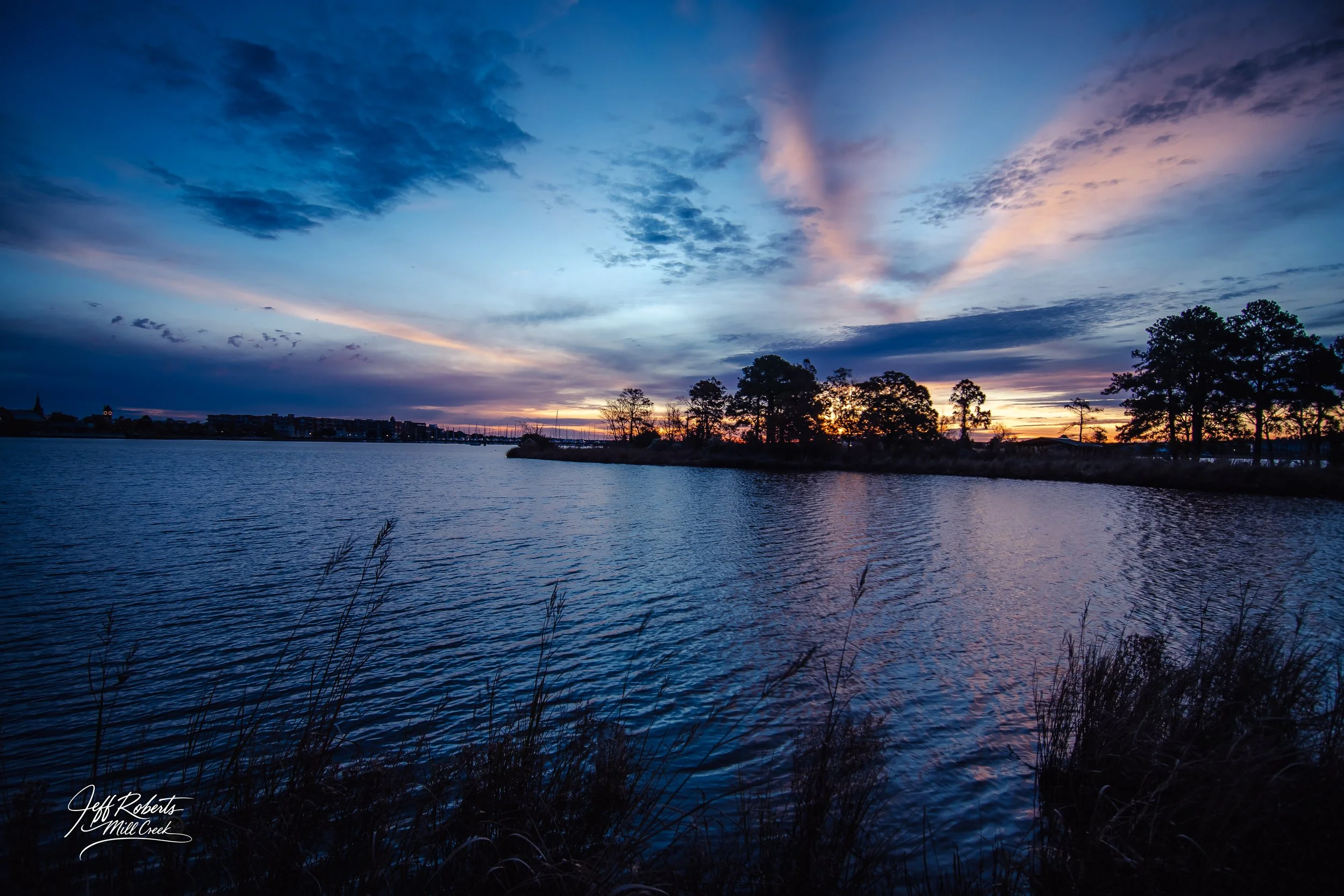 Sunset over a river with silhouettes of trees on the horizon and colorful sky with clouds.