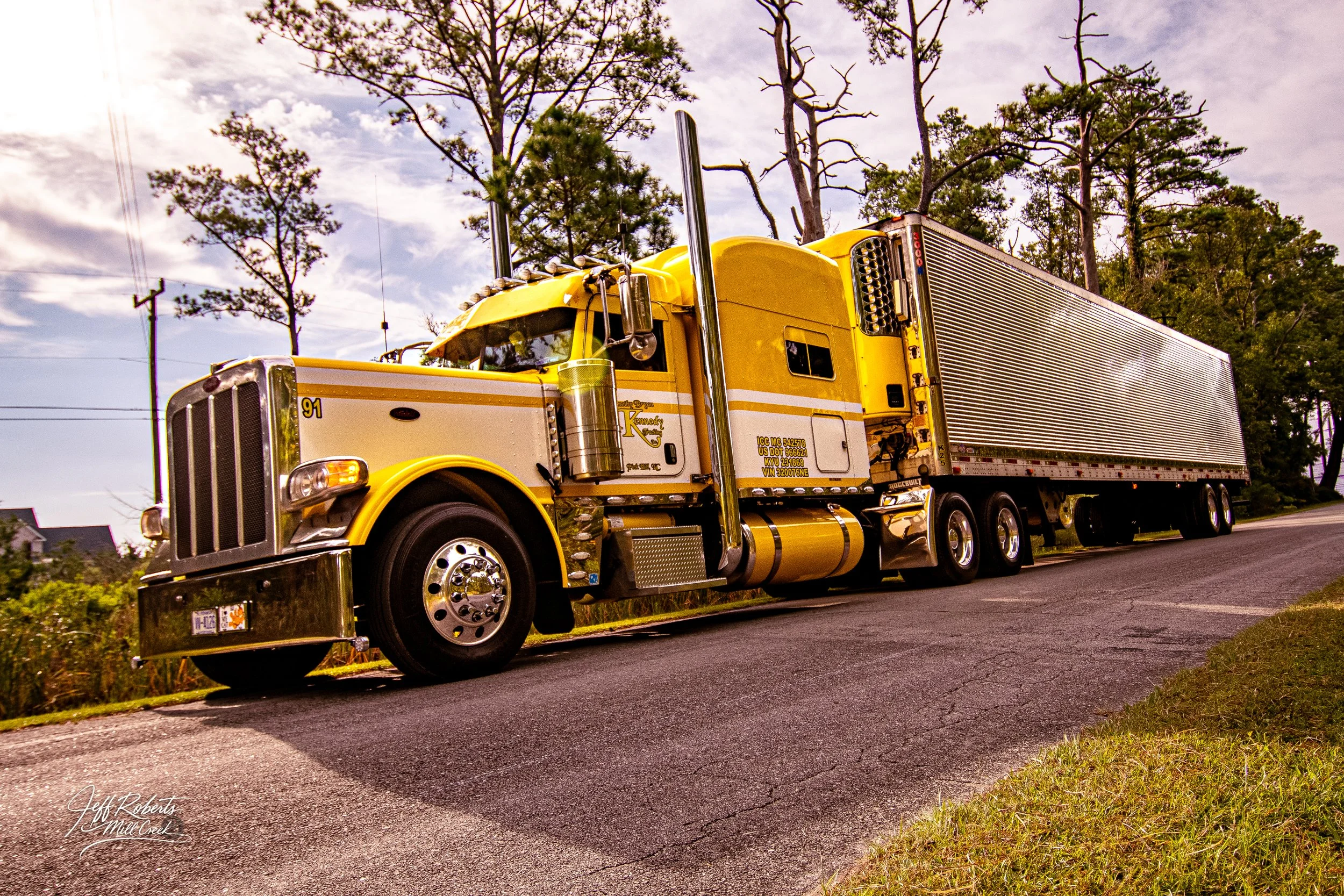 Yellow semi-truck stopped on a rural road with trees and power lines in the background