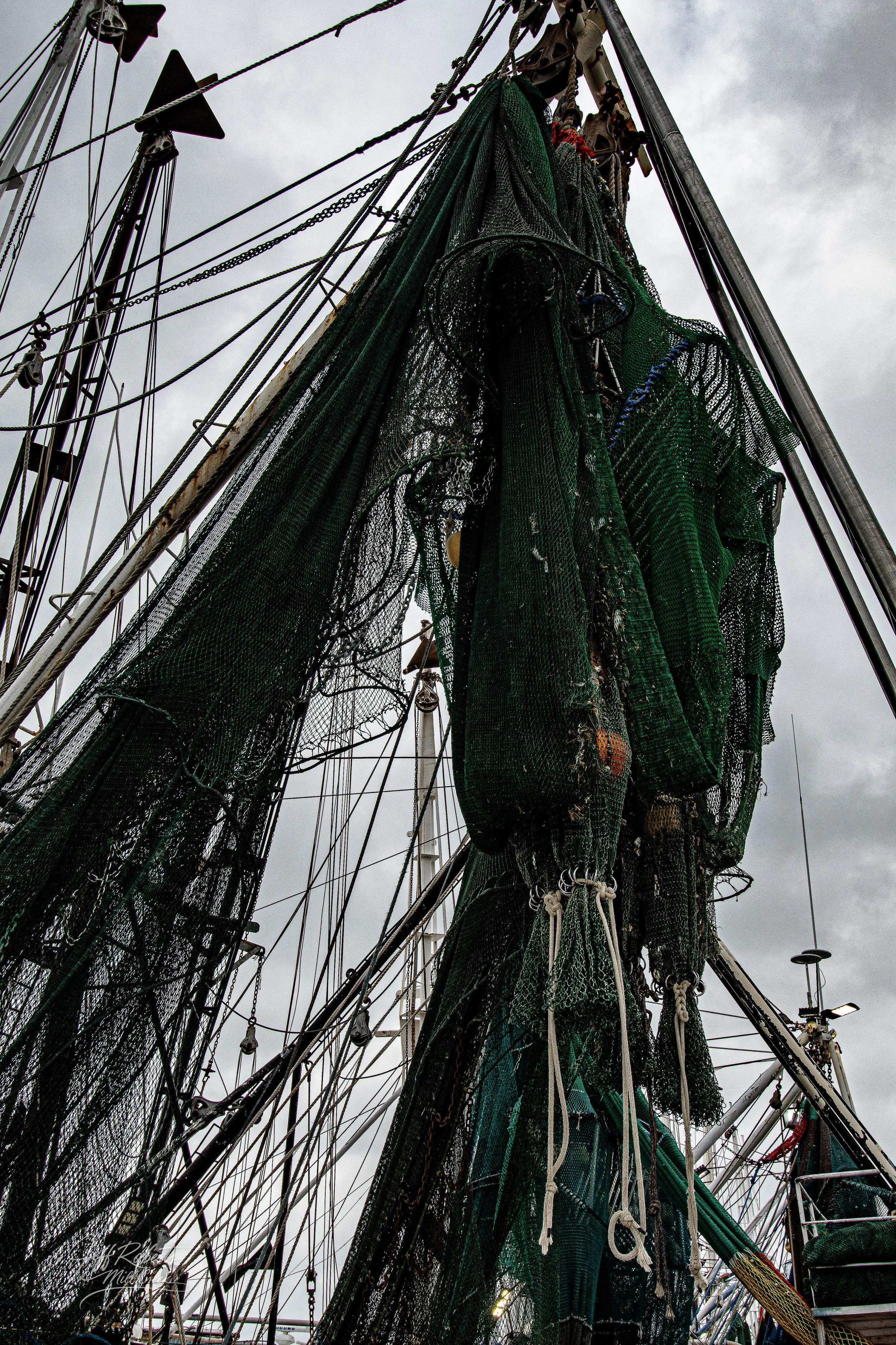 Close-up of stacked fishing nets and ropes on a boat mast on a cloudy day.