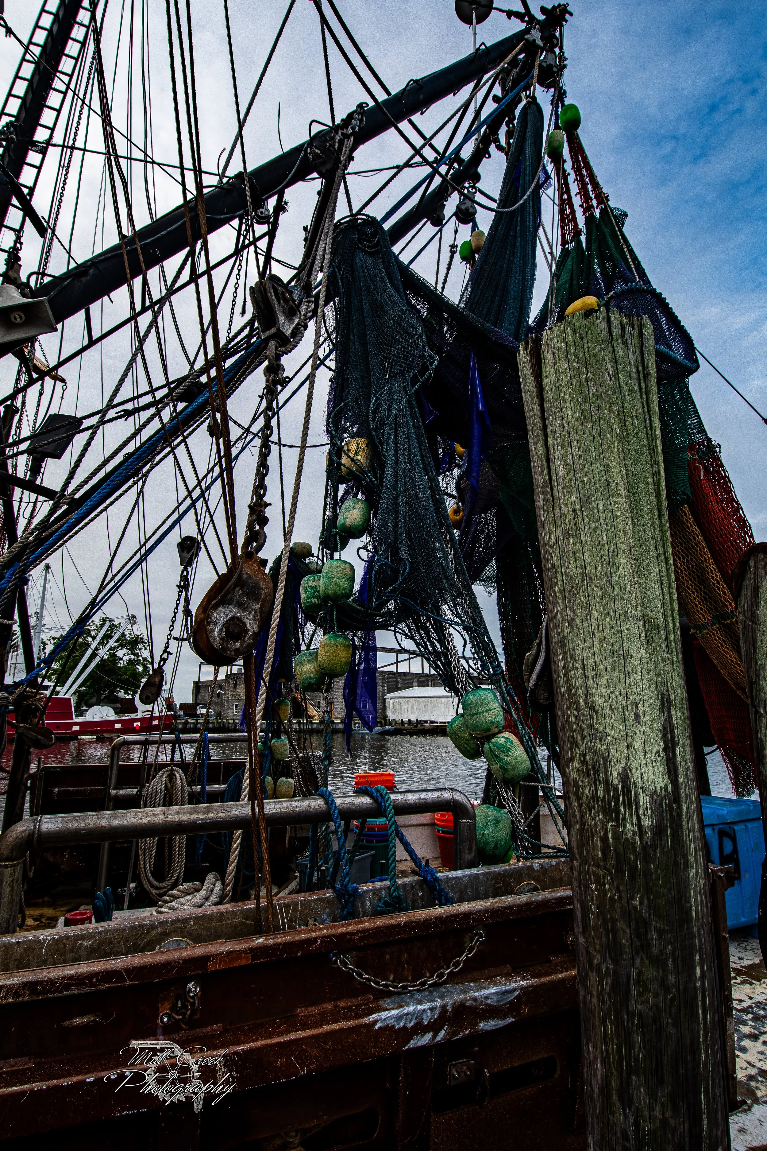 "Nets and Rigging"
Shrimp nets hang heavy with floats, their colors and textures contrasting with the steel rigging and weathered wood pilings of the dockside.