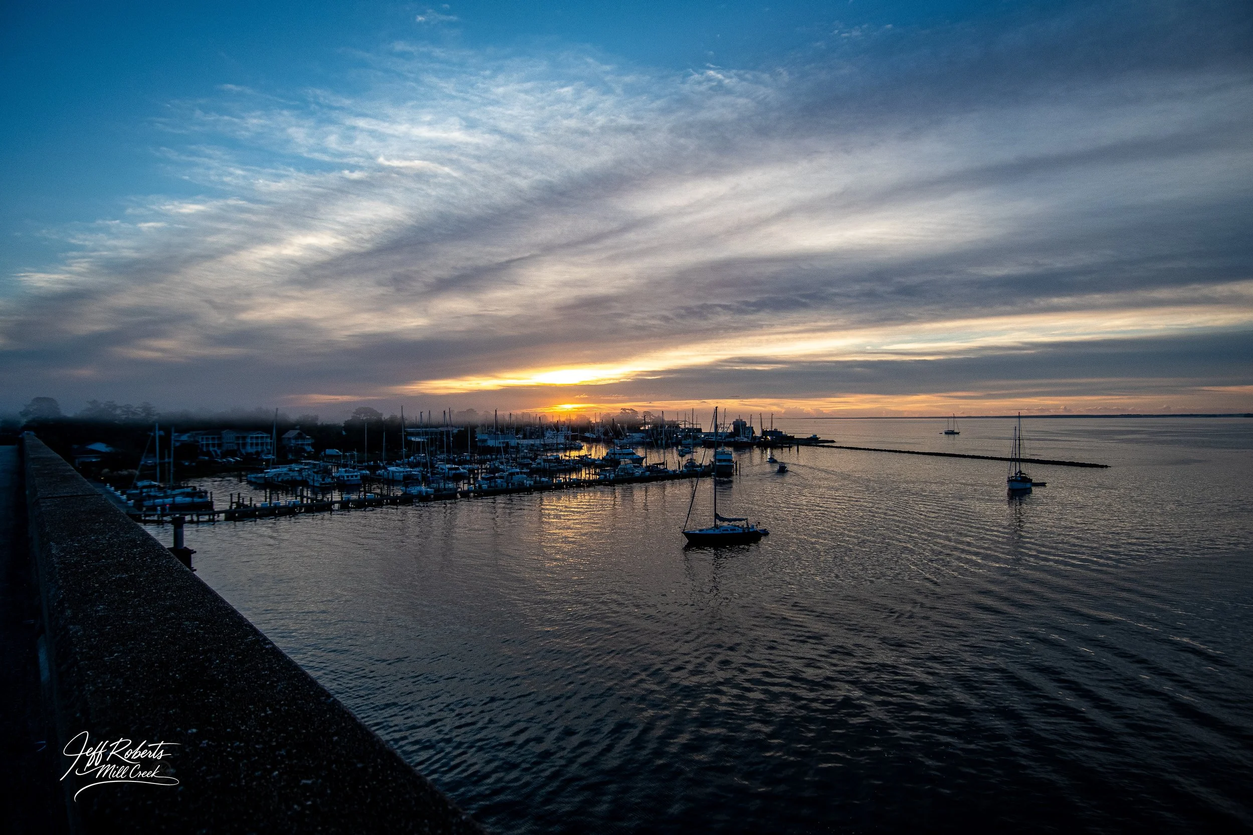Sunset over a marina with boats docked and calm water, partly cloudy sky