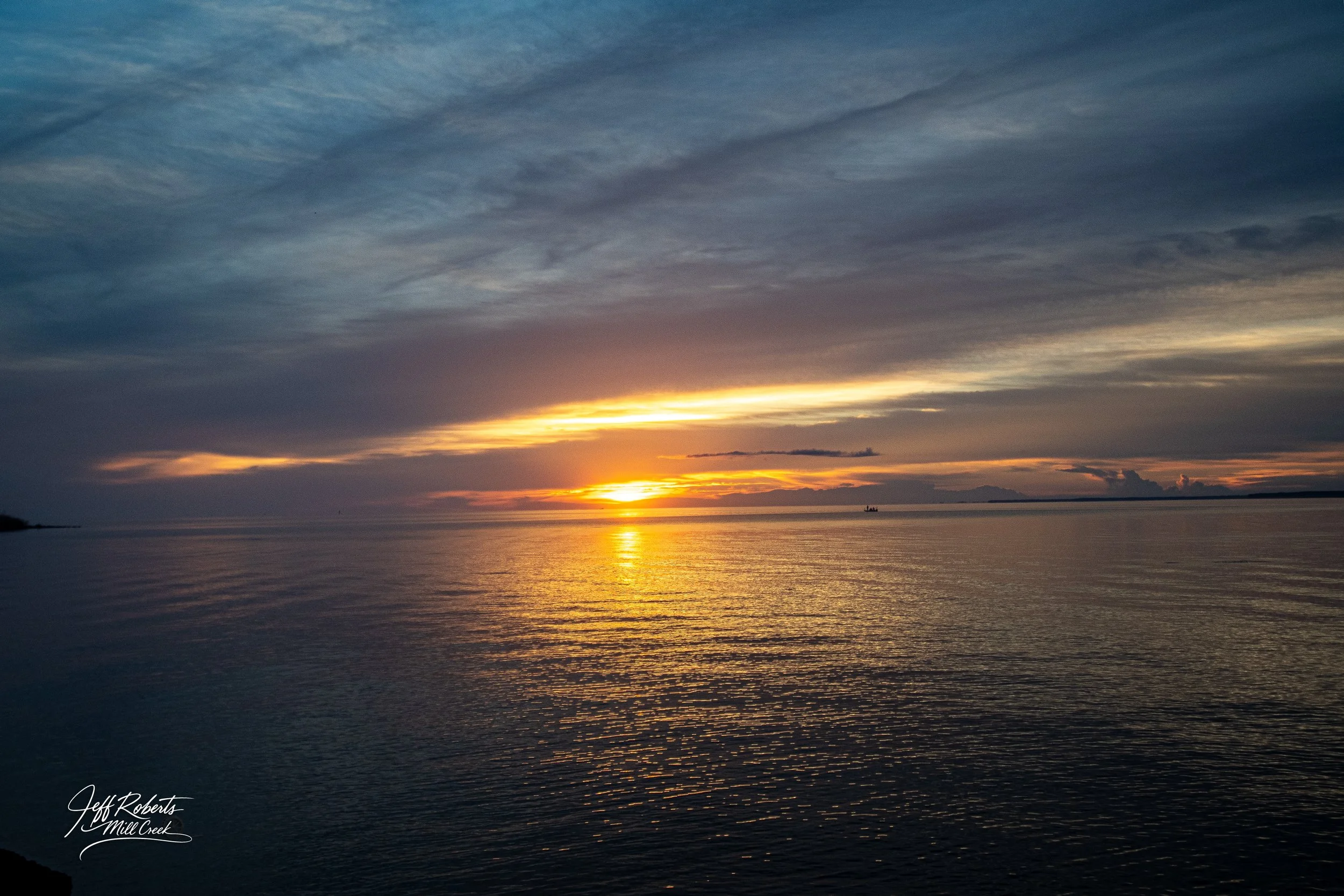 Sunset over a calm body of water with a partly cloudy sky.