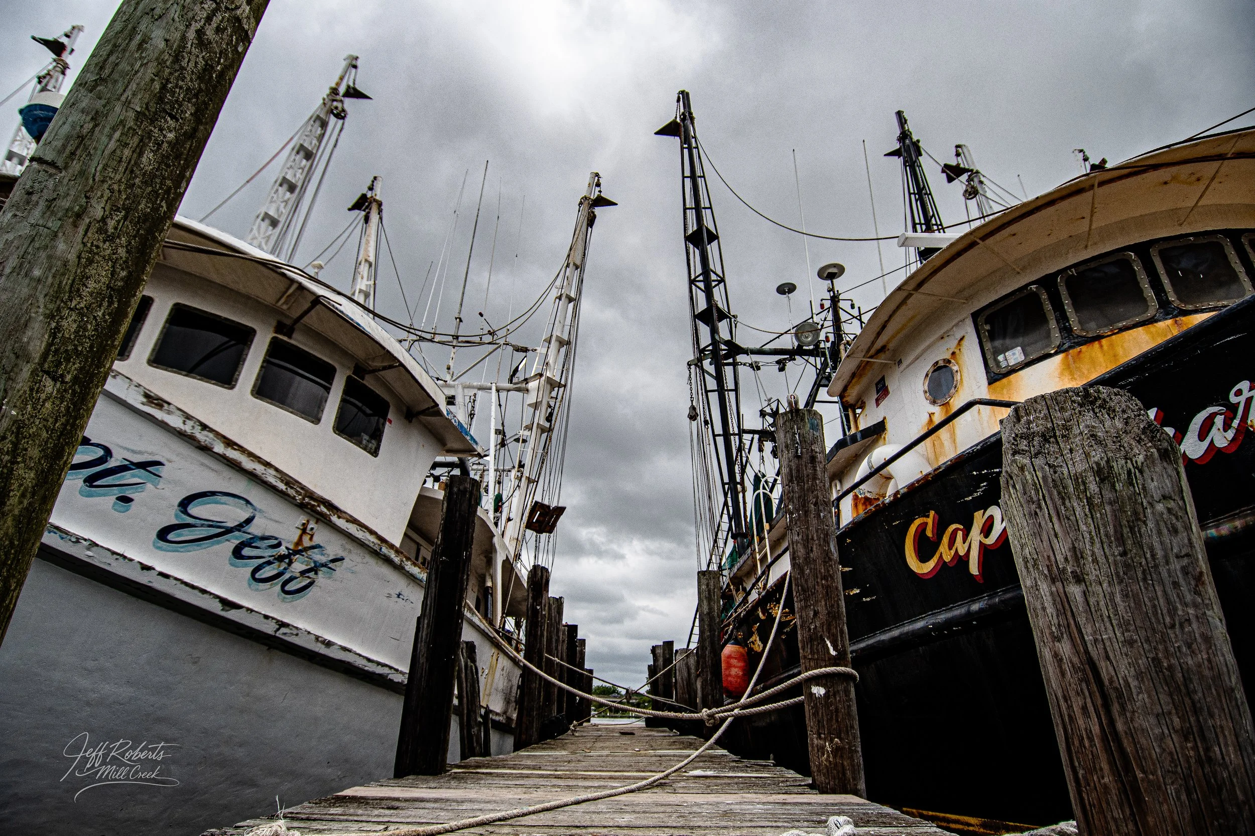 Low-angle view of two old boats docked at a wooden pier on a cloudy day.