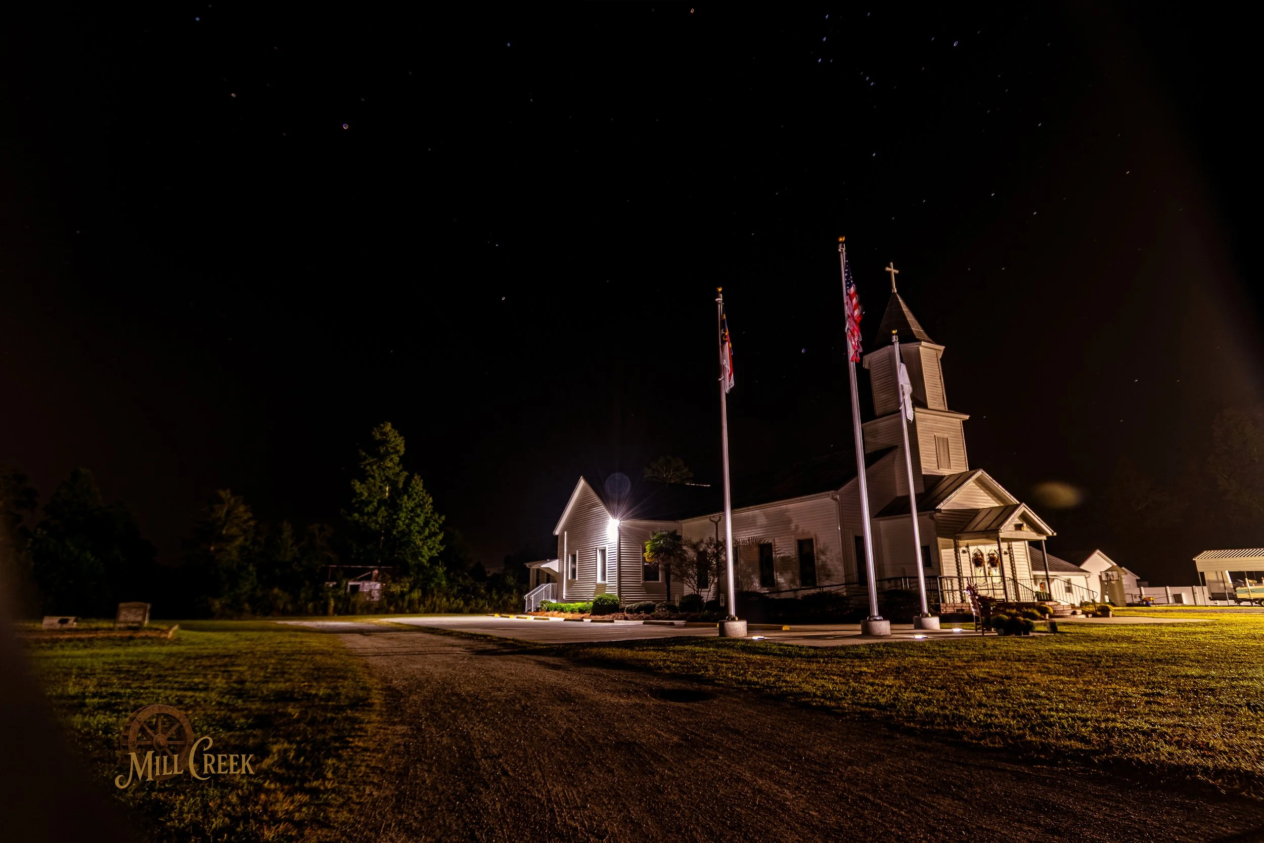 A church illuminated at night with flags in front and a starry sky overhead.