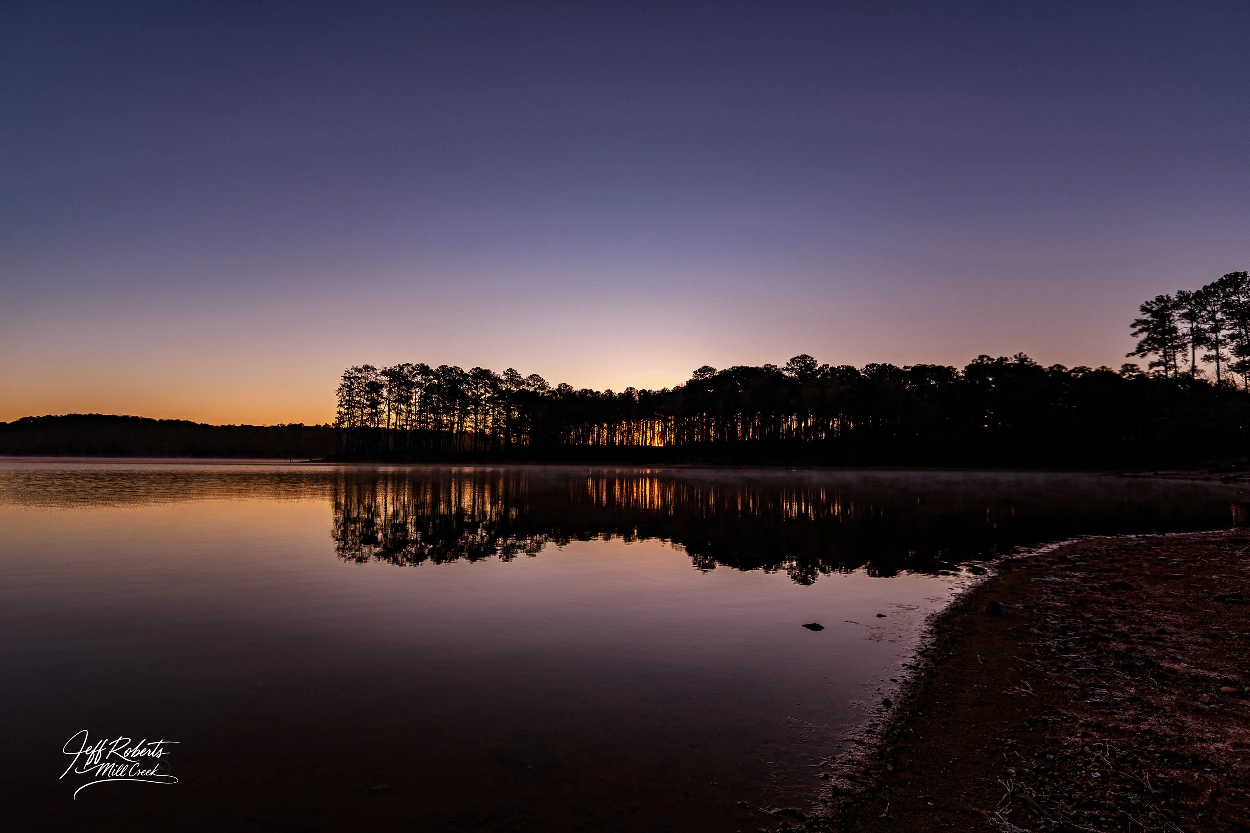Sunset over a calm river with a silhouetted treeline reflected in the water at Mill Creek.