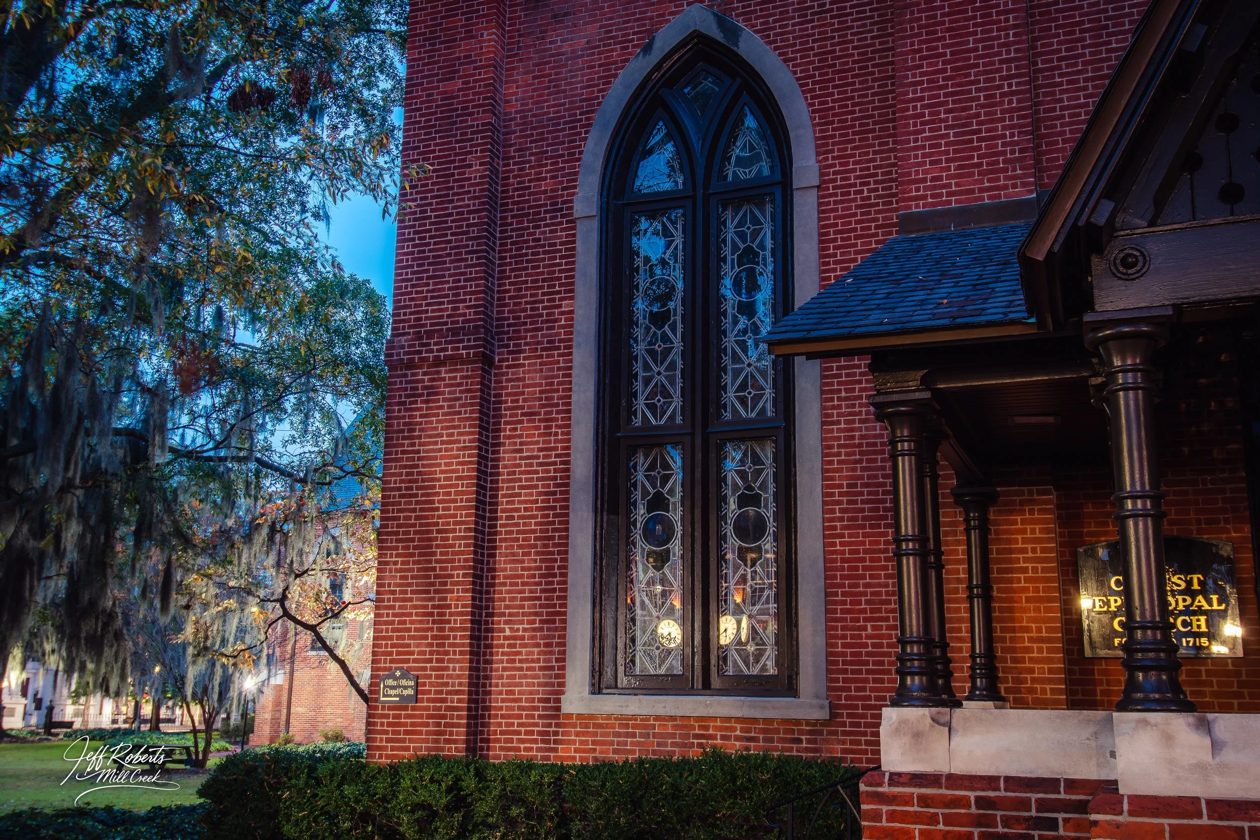 A brick church with a tall arched stained glass window, a small porch with black columns, and a sign that reads 'Christ Episcopal Church, founded 1715.'