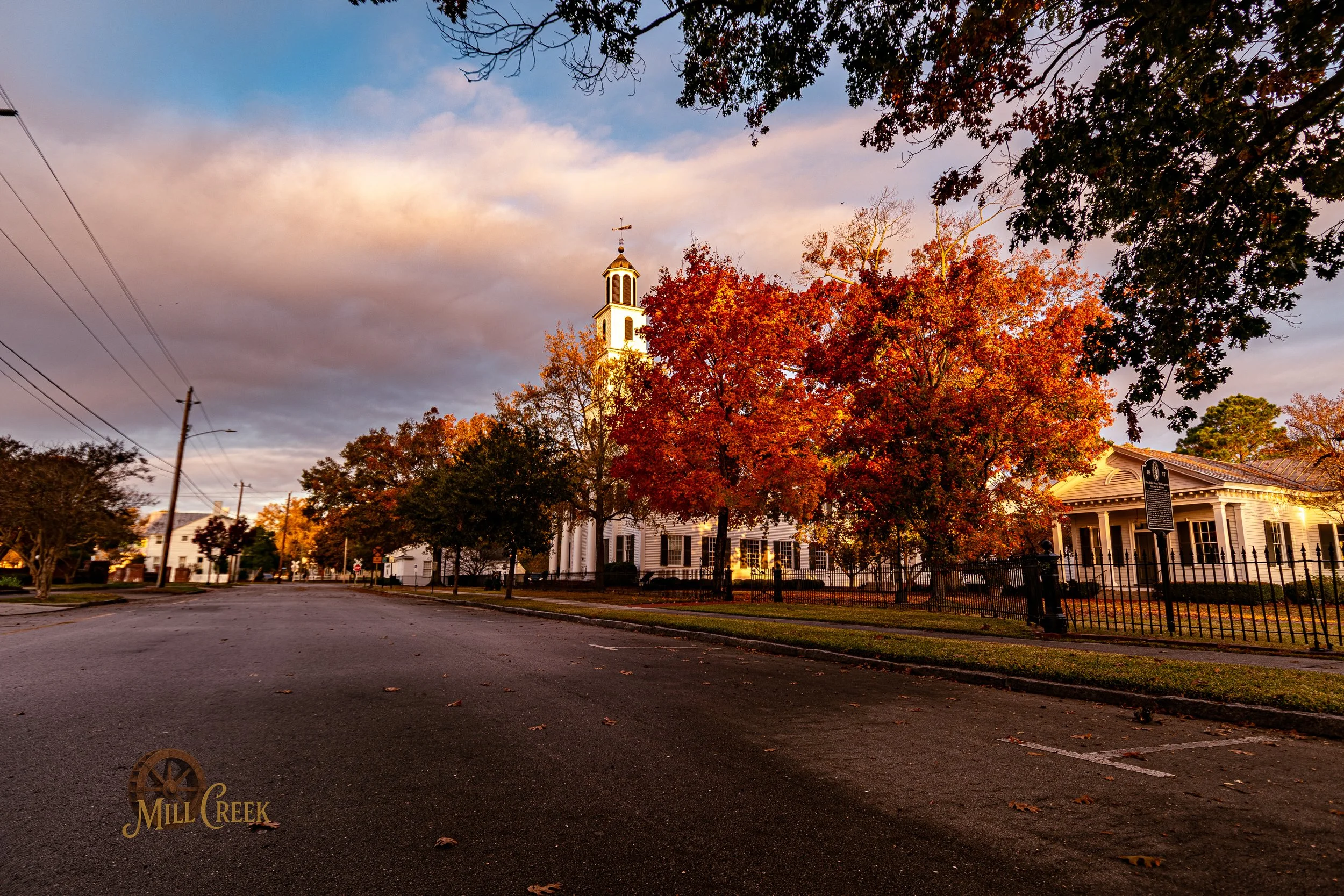 Downtown street at sunset with a white church and orange autumn trees.