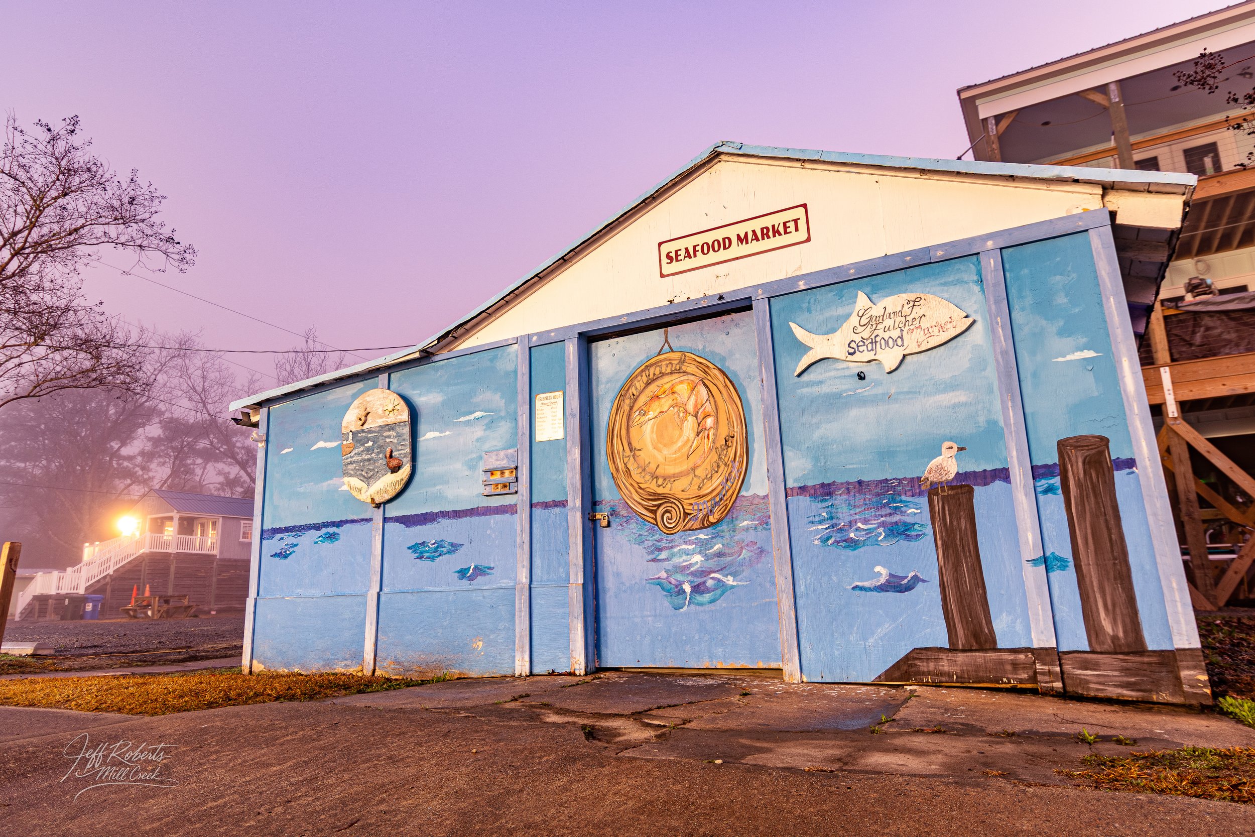 Building with ocean-themed mural, sign reading 'Seafood Market' on the roof, and various painted fish, seagulls, and ocean waves.