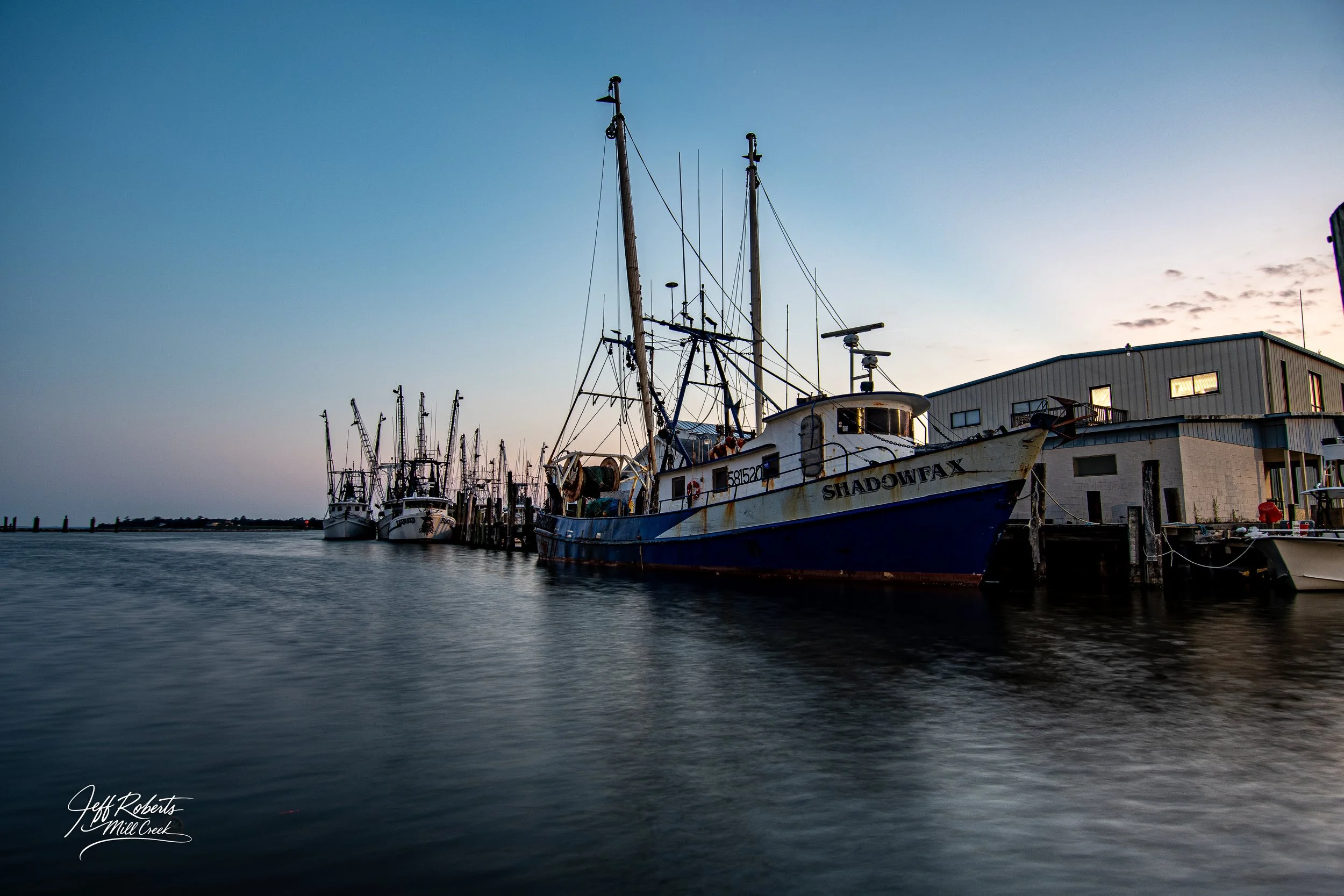 Boats docked along a pier at sunset with a building in the background.
