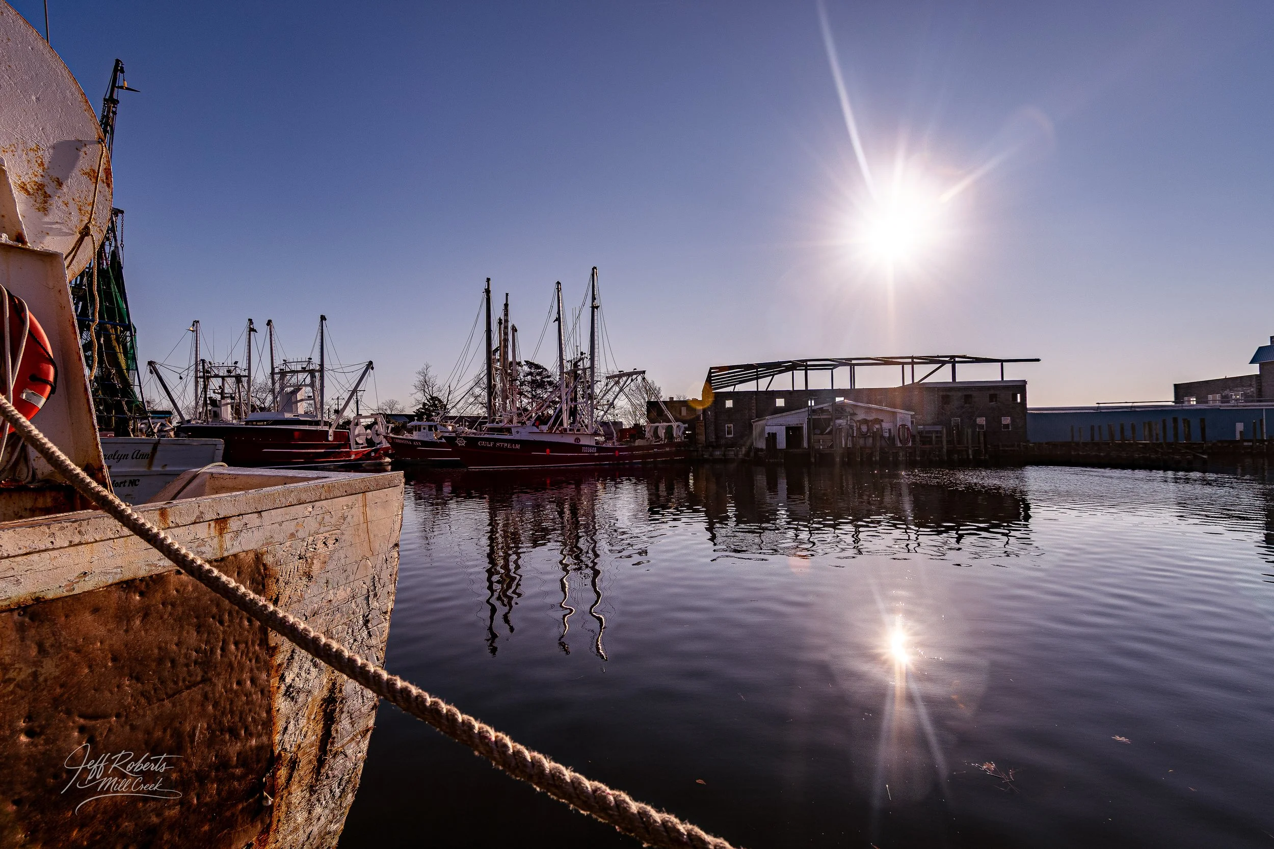 Boats docked at a marina during sunset, with reflections on calm water and clear sky.