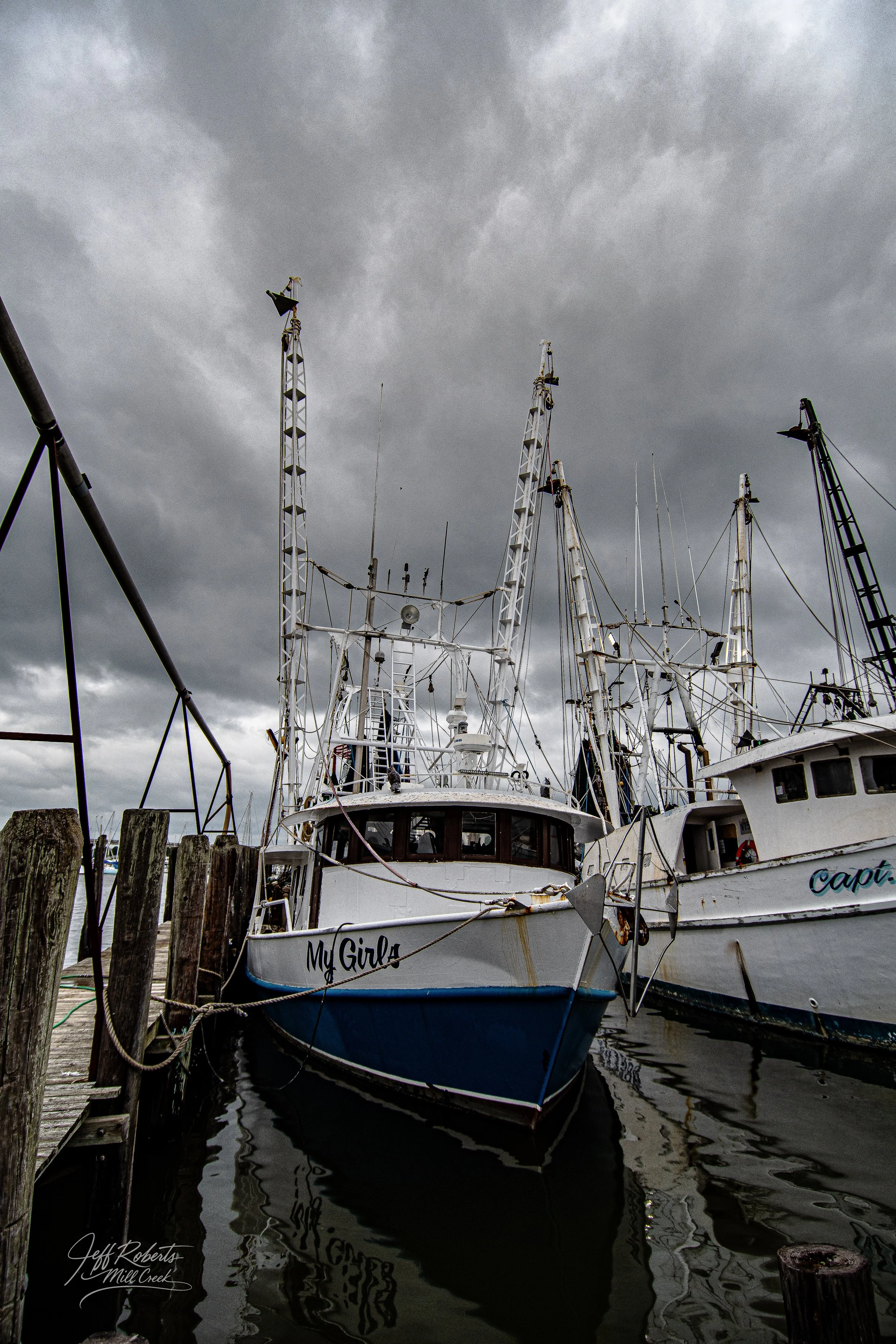 A boat named "My Girl" docked at a marina with other boats, under a cloudy sky.